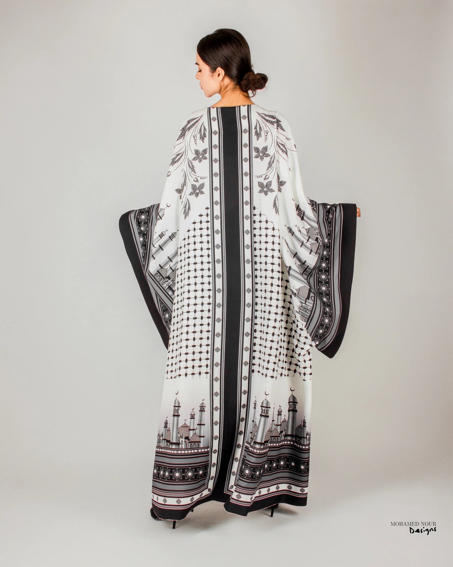 Elegant black and white gown with intricate Palestinian shawl-inspired patterns, featuring mosque motifs and geometric designs. Visit www.mnourdesign.com for more.