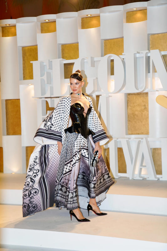 Model in a patterned dress standing in front of a decorative wall with large letters.