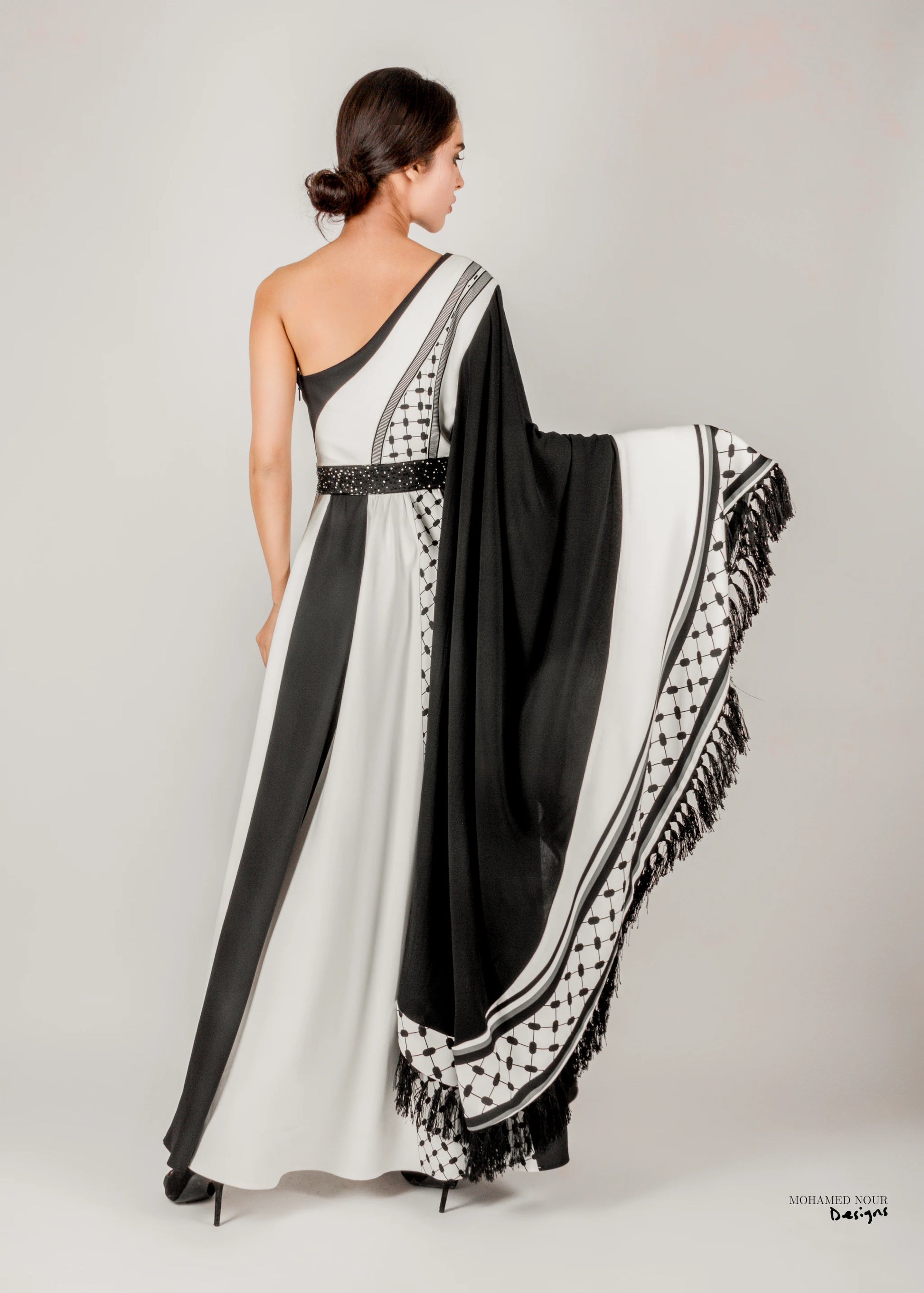 Elegant black and white gown with Palestinian shawl-inspired patterns, featuring geometric designs and fringe details. Visit www.mnourdesign.com for more