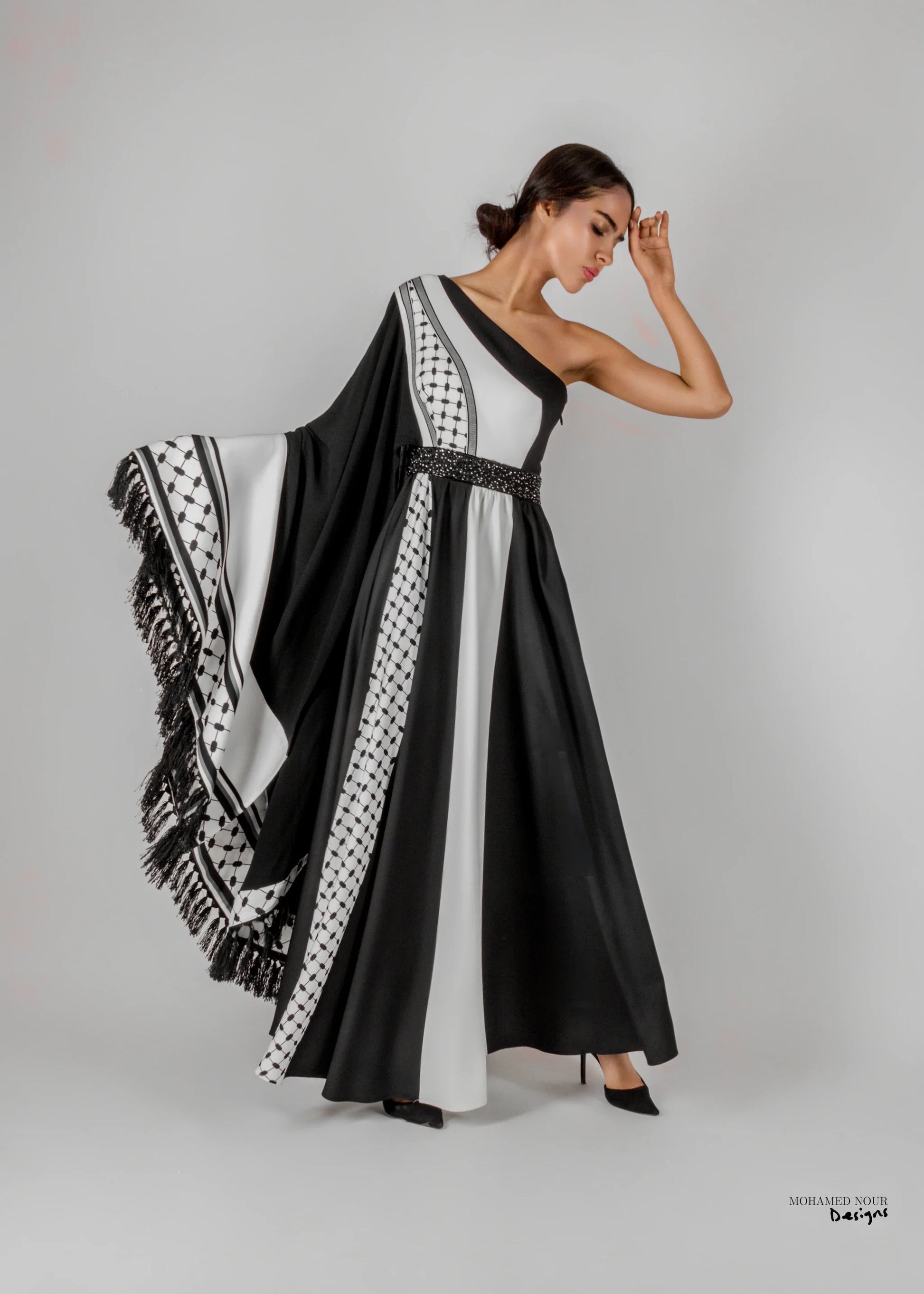 Elegant black and white gown with Palestinian shawl-inspired patterns, featuring geometric designs and fringe details. Visit www.mnourdesign.com for more