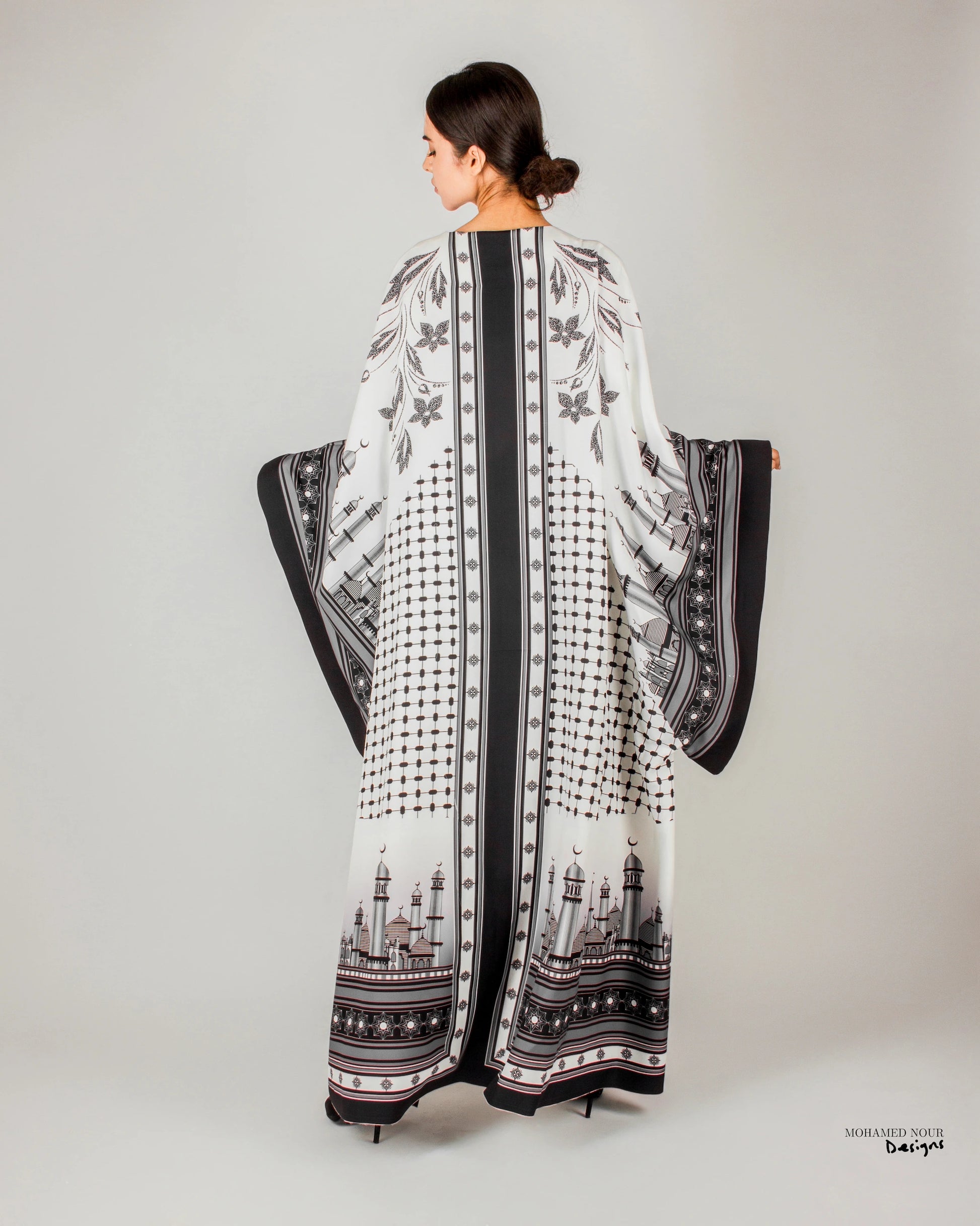 Elegant black and white gown with intricate Palestinian shawl-inspired patterns, featuring mosque motifs and geometric designs. Visit www.mnourdesign.com for more.