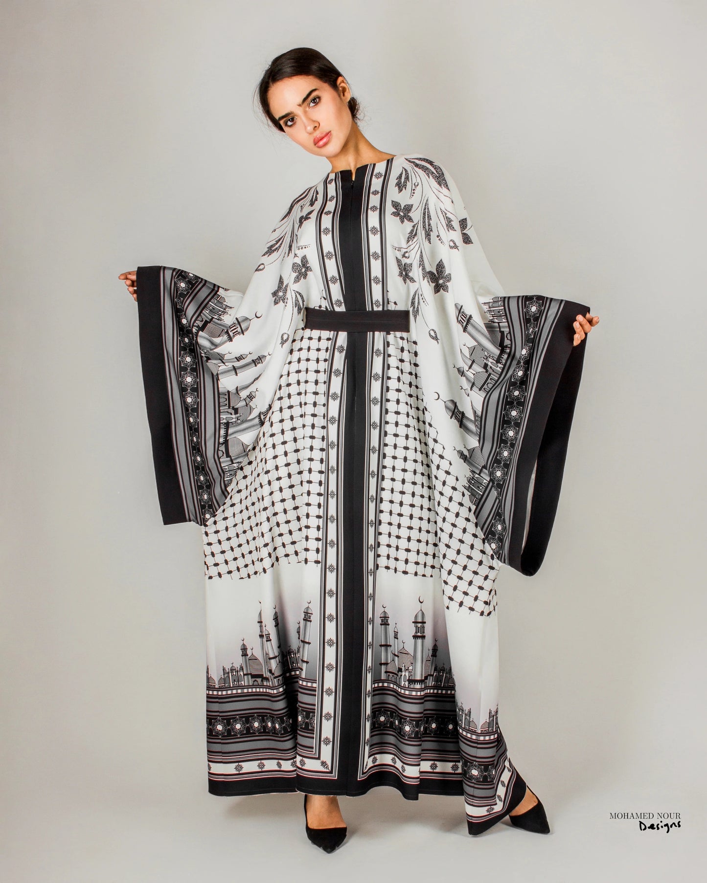 Elegant black and white gown with intricate Palestinian shawl-inspired patterns, featuring mosque motifs and geometric designs. Visit www.mnourdesign.com for more.
