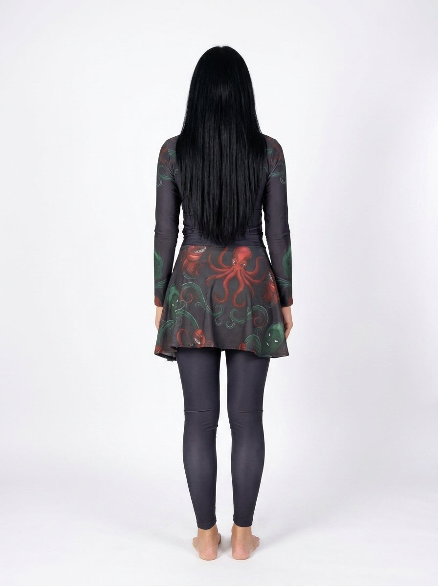 A woman with long black hair is shown from behind wearing a dark gray long-sleeve tunic top with a red and green octopus print, paired with dark gray leggings, against a plain white studio background.