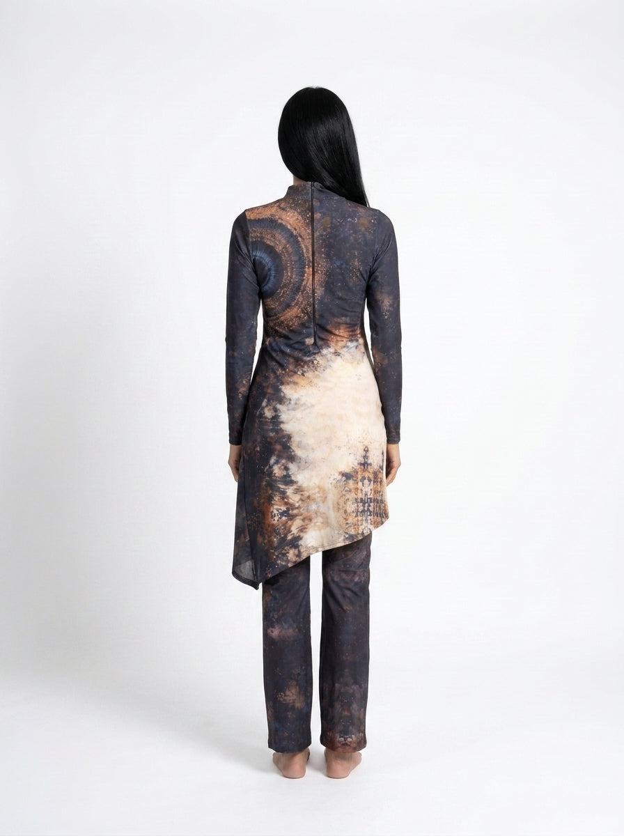 A woman viewed from the back wearing a long-sleeve tunic and trouser set with a dark abstract print in black, brown, and beige, set against a plain white studio background.