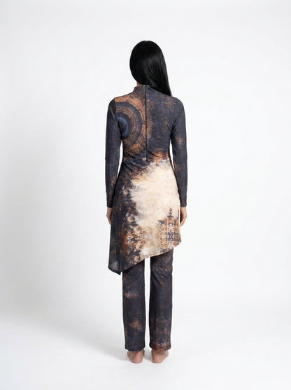 A woman viewed from the back wearing a long-sleeve tunic and trouser set with a dark abstract print in black, brown, and beige, set against a plain white studio background.