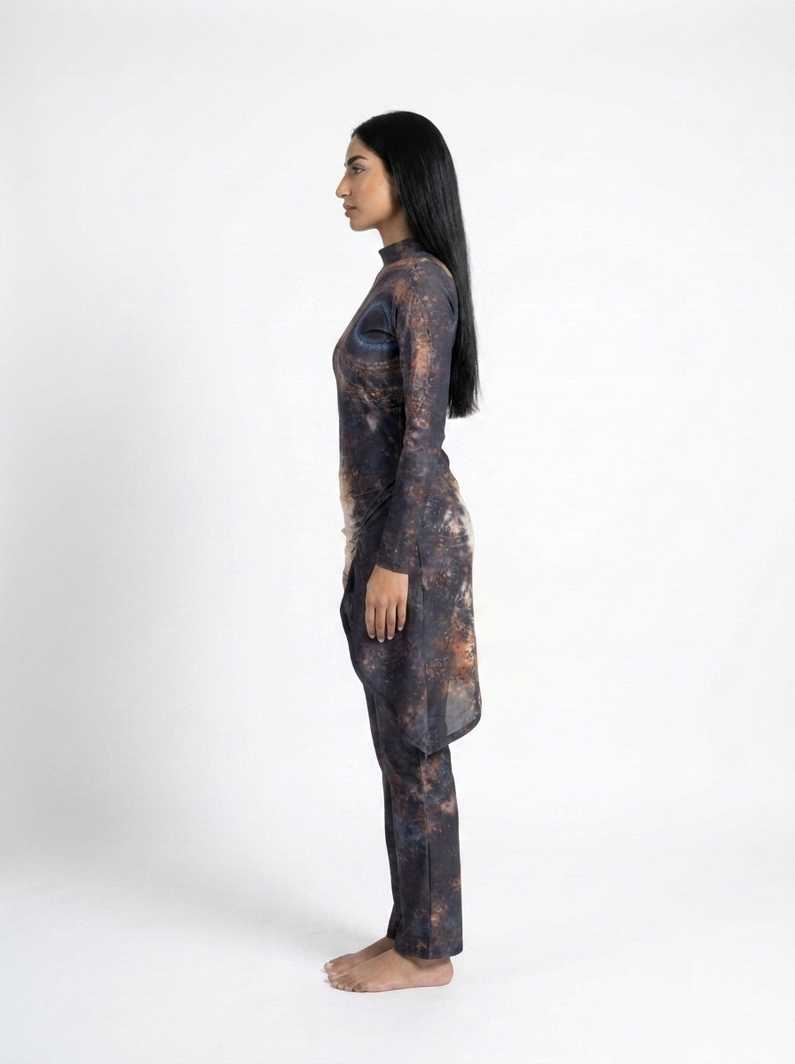 A woman stands in profile against a plain white studio background, wearing a long-sleeve matching set with an abstract dark print in black, gray, and warm brown tones.