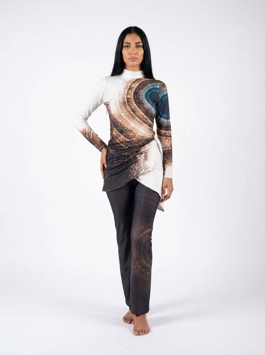 A woman modeling a long-sleeve asymmetrical top and matching pants set. The top features a white shoulder and sleeve with a large abstract spiral print in brown, beige, and blue-gray across the torso.