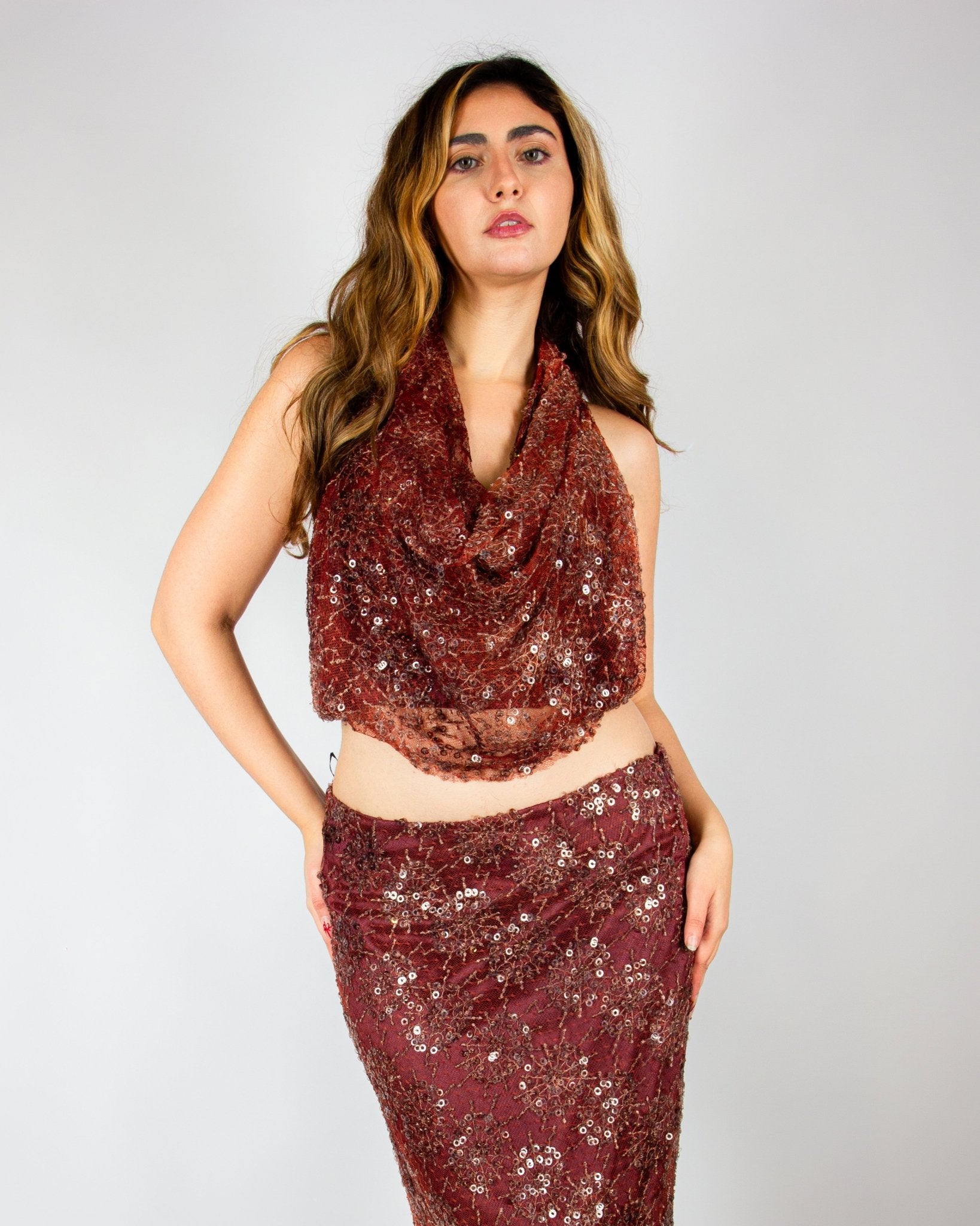Elegant two-piece evening ensemble by MNour Design, featuring a shimmering burgundy sequined skirt with a high slit and a draped cowl-neck crop top. The intricate beadwork and rich fabric exude sophistication and modern glamour. Shop this exclusive design at www.mnourdesign.com