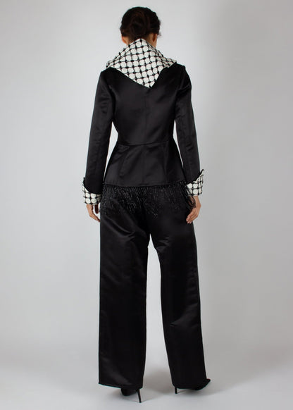 Elegant black satin pantsuit from the HORRA collection by MNour Design, featuring a statement keffiyeh-inspired lapel and cuff details. The tailored blazer is adorned with intricate beaded fringe, adding a touch of modern sophistication. Discover more at www.mnourdesign.com