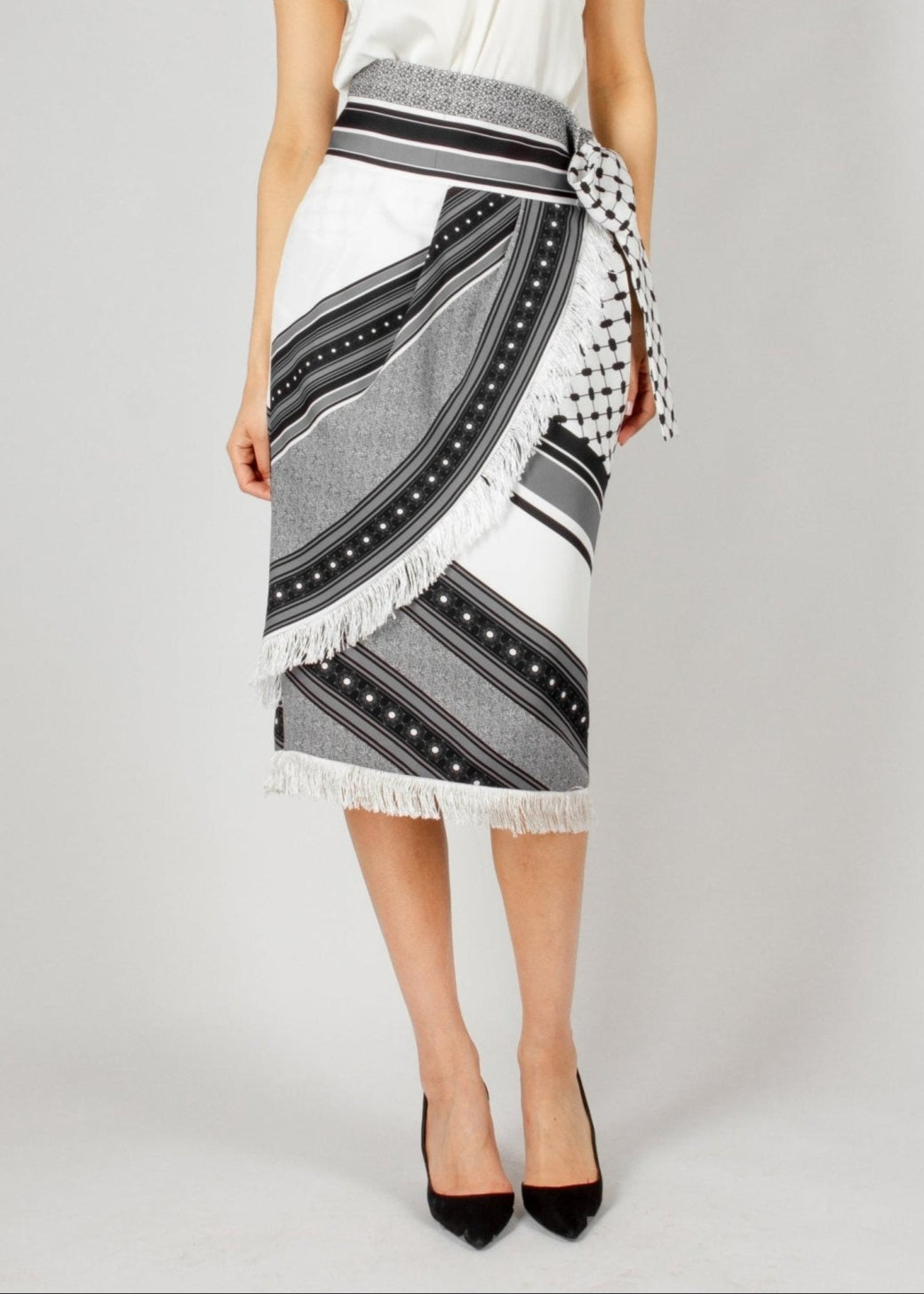Chic wrap-style midi skirt from the HORRA collection by MNour Design, featuring a striking black-and-white traditional pattern with fringe detailing and a statement side tie. Paired with a sleek satin top and classic heels for an effortlessly elegant look. Explore more at www.mnourdesign.com