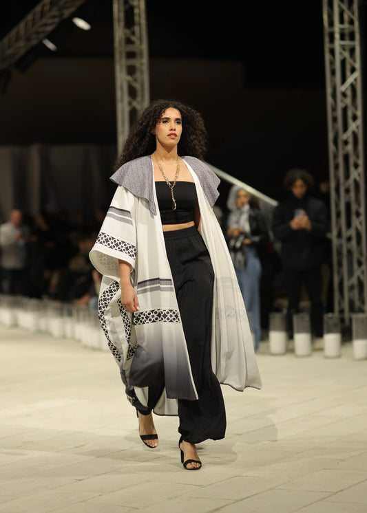 A striking black and white gradient kimono from the HORRA collection by MNour Design, showcased on the runway. Featuring traditional Palestinian keffiyeh-inspired patterns with a modern ombre effect, this elegant piece flows effortlessly, blending heritage with contemporary fashion. Explore the collection at www.mnourdesign.com