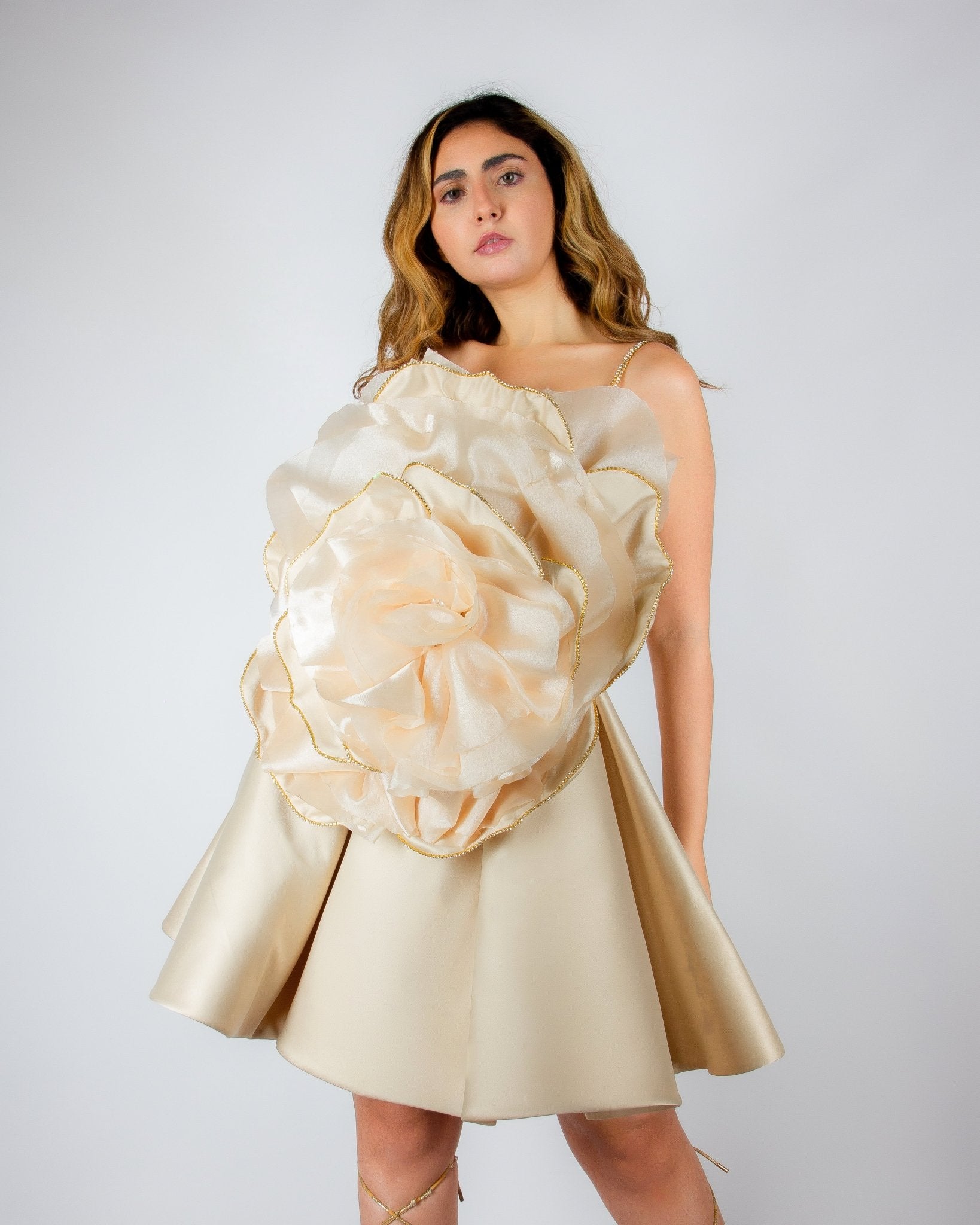 Luxurious champagne-colored mini dress by MNour Design, featuring a voluminous satin skirt and an oversized sculptural rose detail on the bodice with gold-trimmed petals. A bold, artistic statement for elegant occasions. Discover this exclusive couture piece at www.mnourdesign.com.
