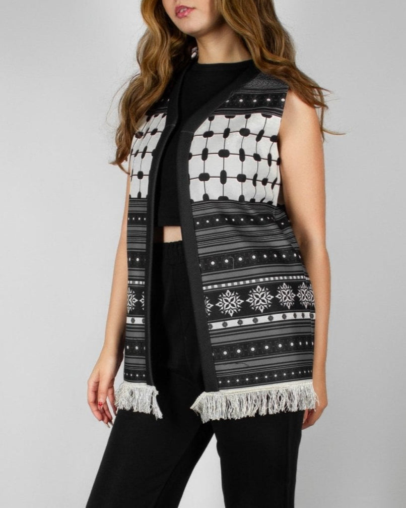 Modern black and white vest from the HORRA collection by MNour Design, featuring intricate geometric and traditional patterns with delicate fringe detailing. Styled over a sleek black ensemble for a contemporary yet culturally inspired look. Discover more at www.mnourdesign.com