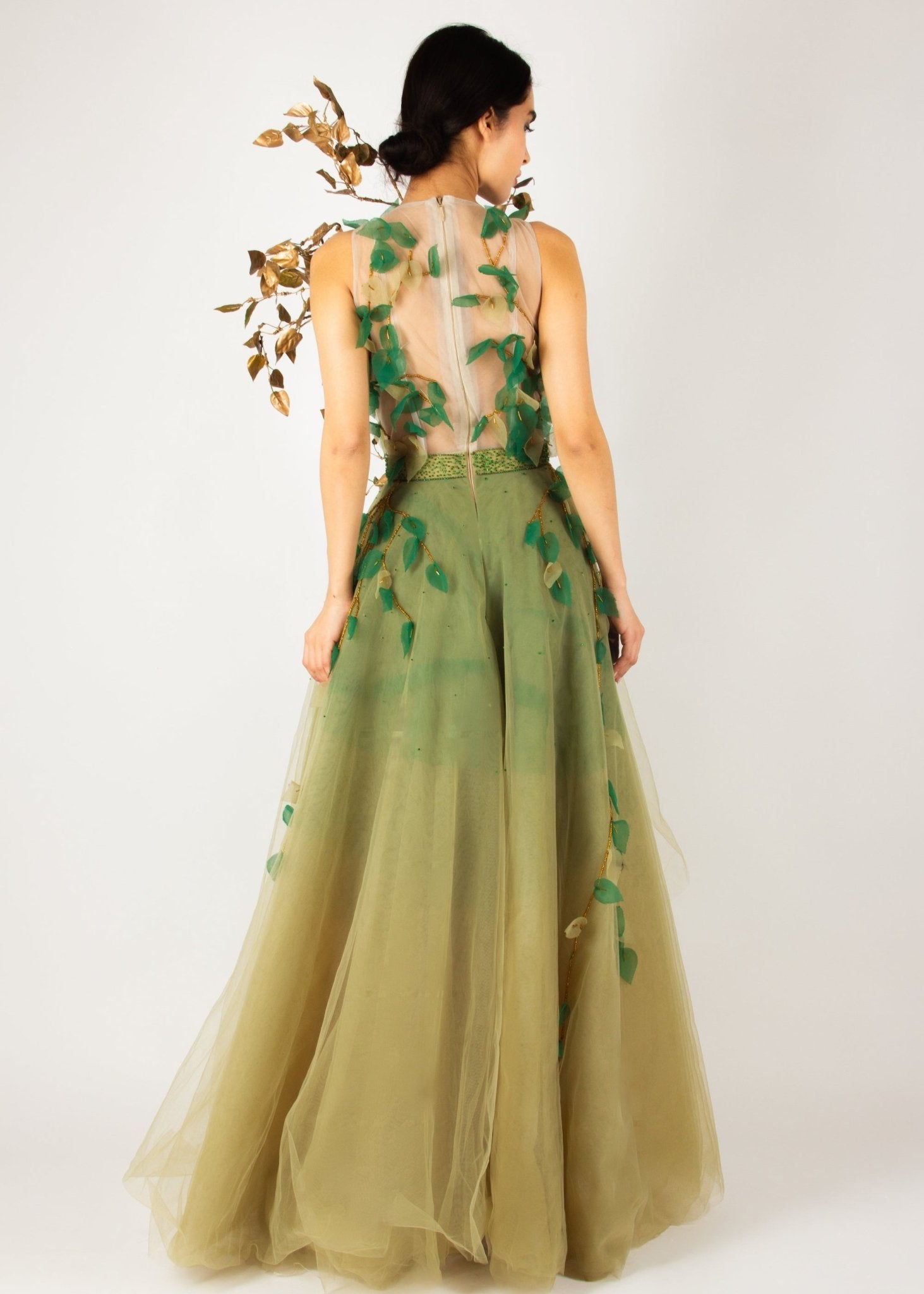 Enchanting nature-inspired gown by MNour Design, featuring a flowing olive-green tulle skirt with a high-low cut and an intricately designed bodice adorned with gold and green leaf appliqués. A breathtaking fusion of fashion and artistry. Discover this exclusive design at www.mnourdesign.com