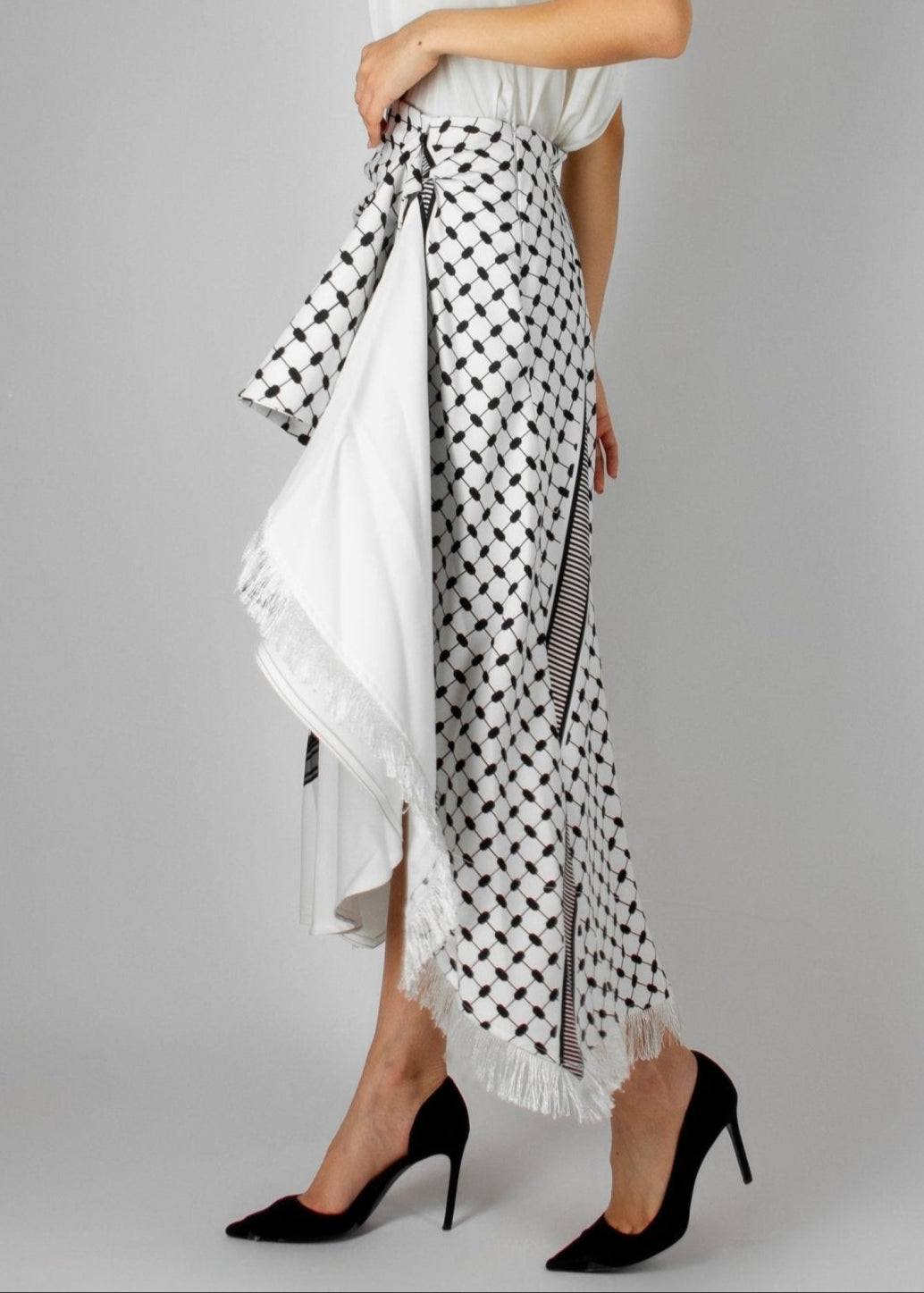 Contemporary white and black asymmetric skirt from the HORRA collection by MNour Design, featuring keffiyeh-inspired patterns and delicate fringe details. Paired with a sleek white sleeveless top for a modern yet culturally rooted look. Explore the collection at www.mnourdesign.com