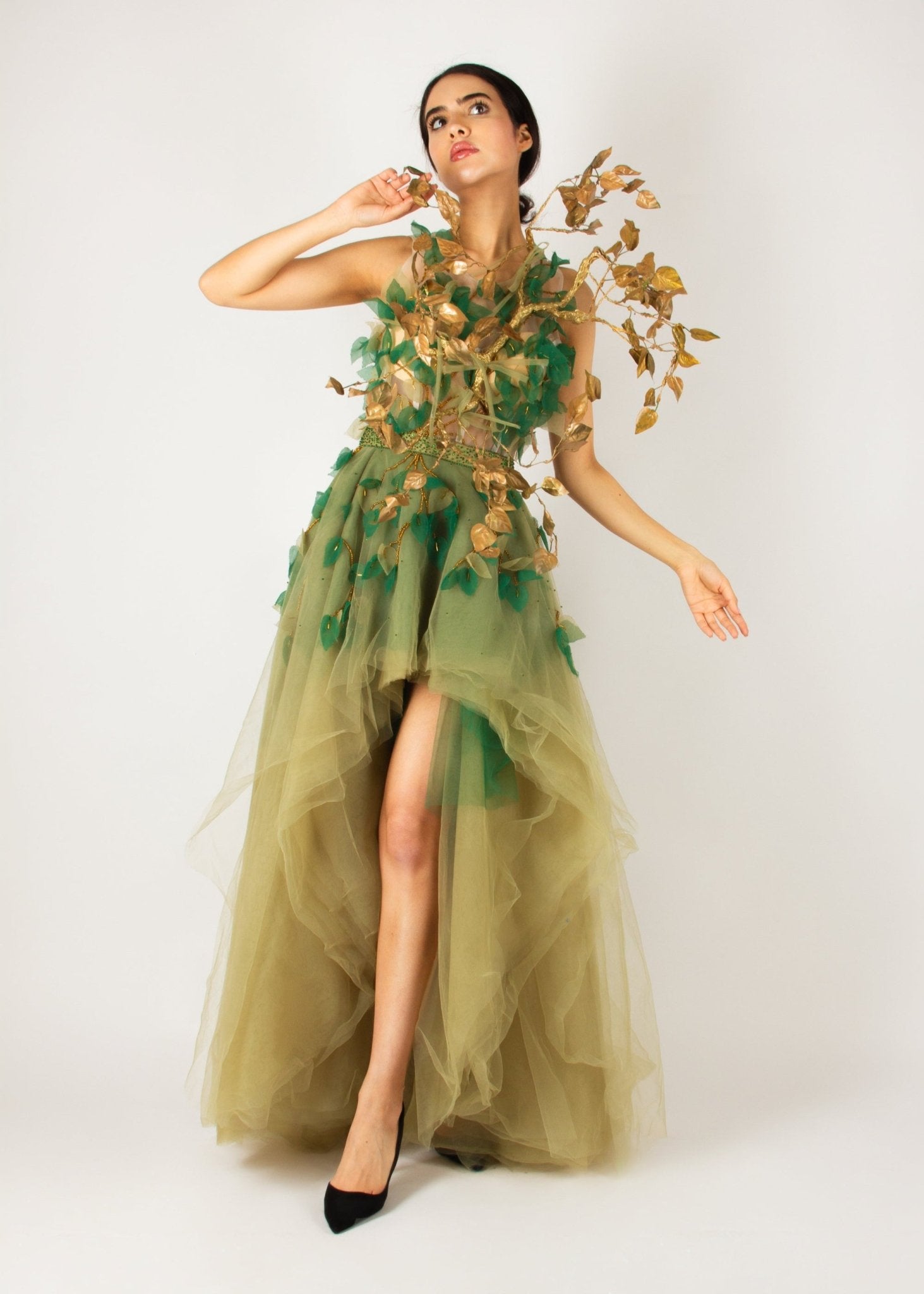 Enchanting nature-inspired gown by MNour Design, featuring a flowing olive-green tulle skirt with a high-low cut and an intricately designed bodice adorned with gold and green leaf appliqués. A breathtaking fusion of fashion and artistry. Discover this exclusive design at www.mnourdesign.com