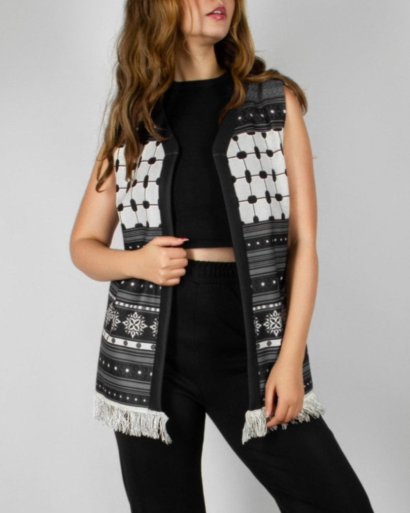 Modern black and white vest from the HORRA collection by MNour Design, featuring intricate geometric and traditional patterns with delicate fringe detailing. Styled over a sleek black ensemble for a contemporary yet culturally inspired look. Discover more at www.mnourdesign.com