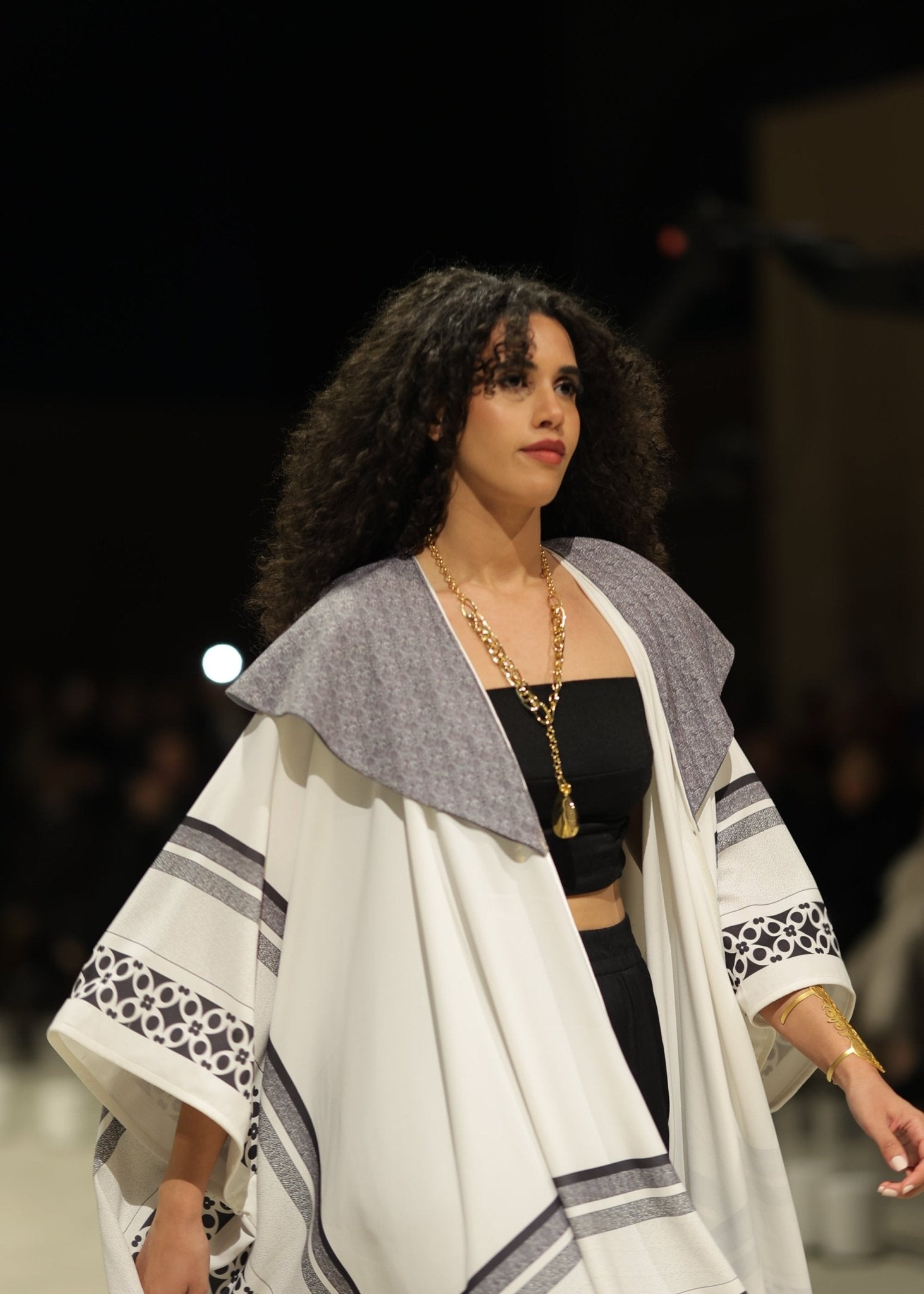 A striking black and white gradient kimono from the HORRA collection by MNour Design, showcased on the runway. Featuring traditional Palestinian keffiyeh-inspired patterns with a modern ombre effect, this elegant piece flows effortlessly, blending heritage with contemporary fashion. Explore the collection at www.mnourdesign.com