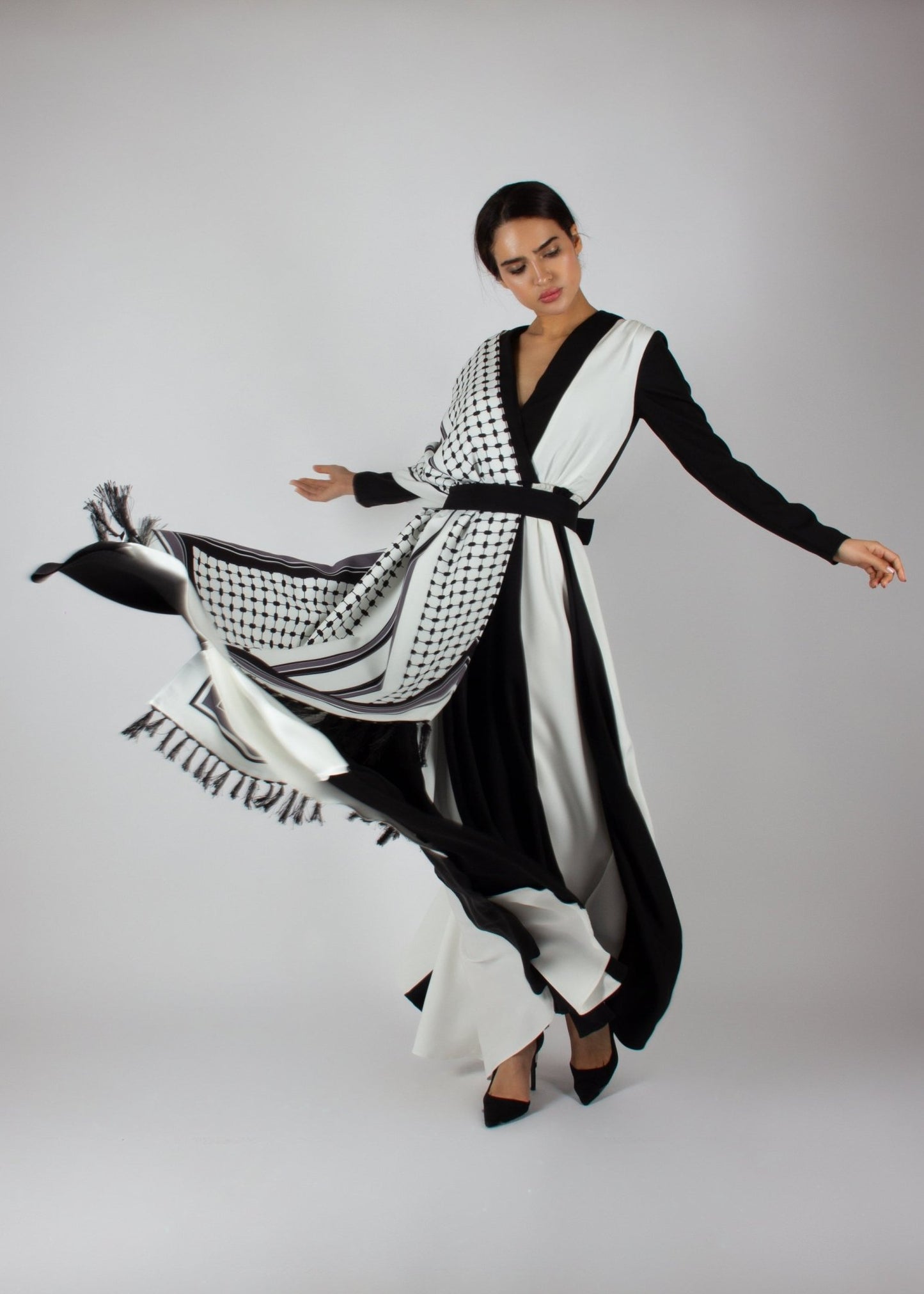 Flowing black and white wrap dress from the HORRA collection by MNour Design, featuring keffiyeh-inspired prints and elegant fringe details. A statement piece blending cultural heritage with modern sophistication. Discover more at www.mnourdesign.com