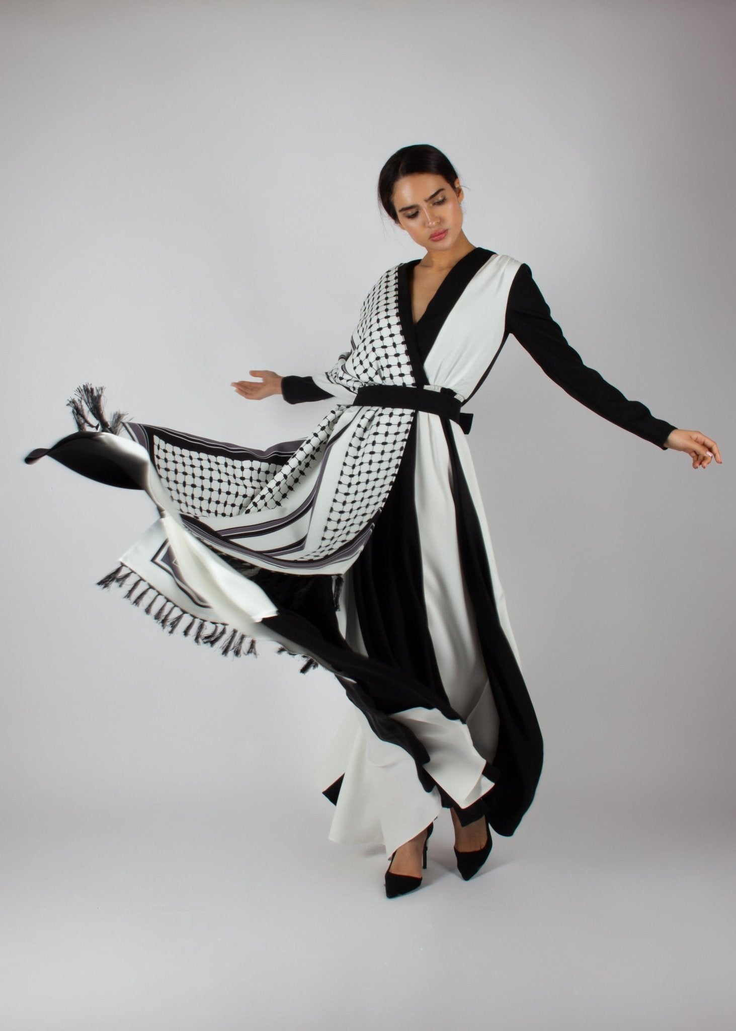 Flowing black and white wrap dress from the HORRA collection by MNour Design, featuring keffiyeh-inspired prints and elegant fringe details. A statement piece blending cultural heritage with modern sophistication. Discover more at www.mnourdesign.com