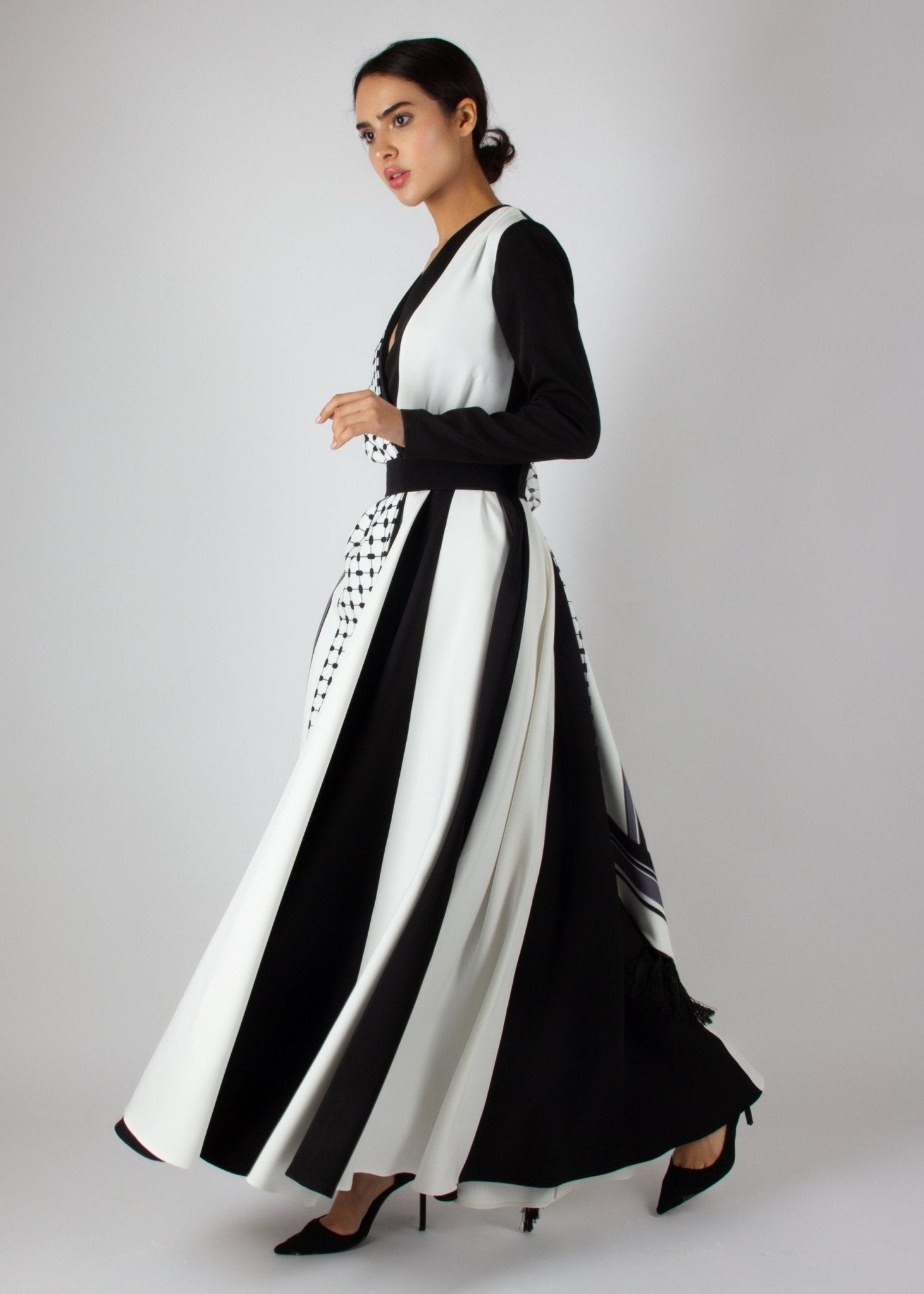 Flowing black and white wrap dress from the HORRA collection by MNour Design, featuring keffiyeh-inspired prints and elegant fringe details. A statement piece blending cultural heritage with modern sophistication. Discover more at www.mnourdesign.com