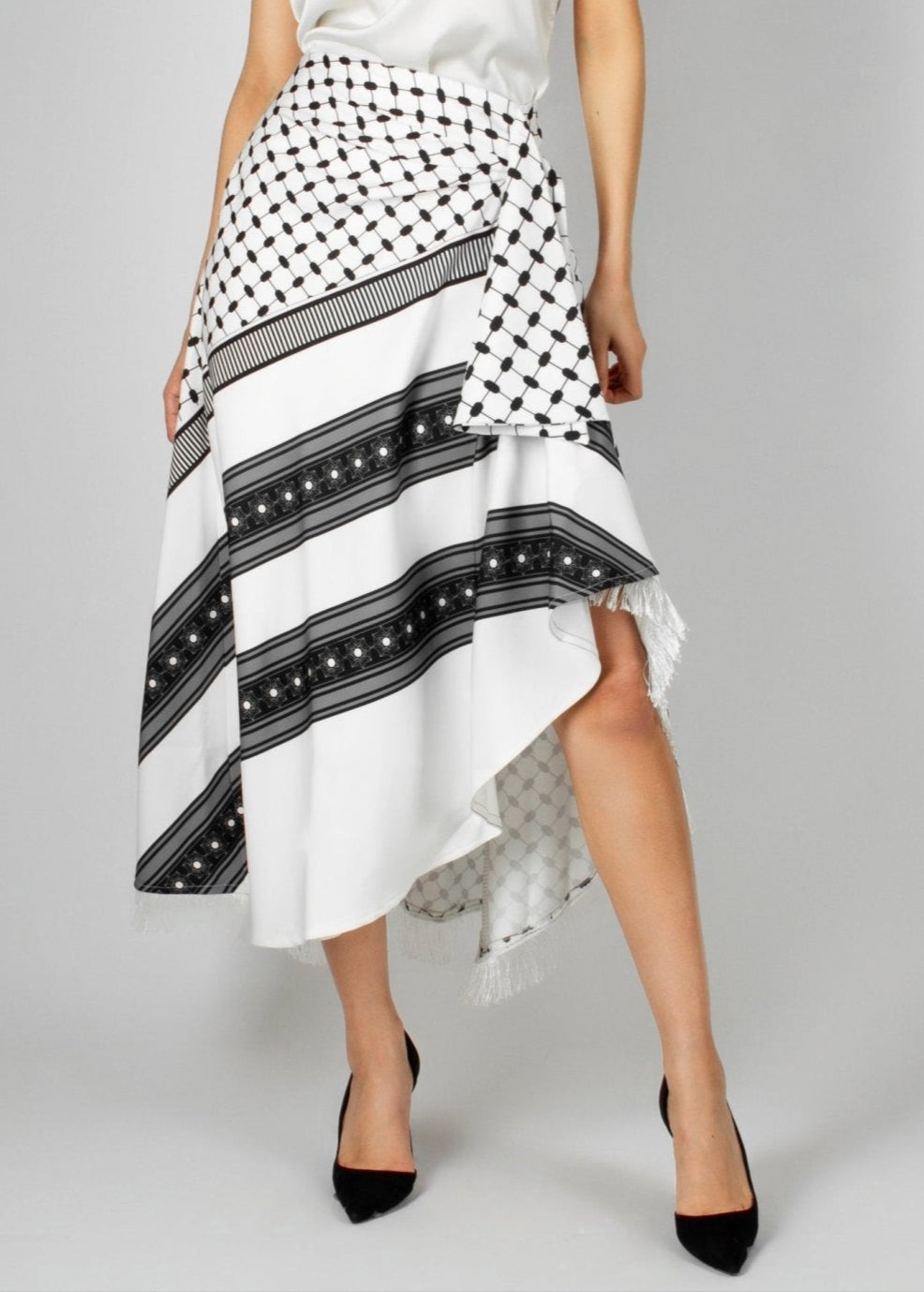 Contemporary white and black asymmetric skirt from the HORRA collection by MNour Design, featuring keffiyeh-inspired patterns and delicate fringe details. Paired with a sleek white sleeveless top for a modern yet culturally rooted look. Explore the collection at www.mnourdesign.com
