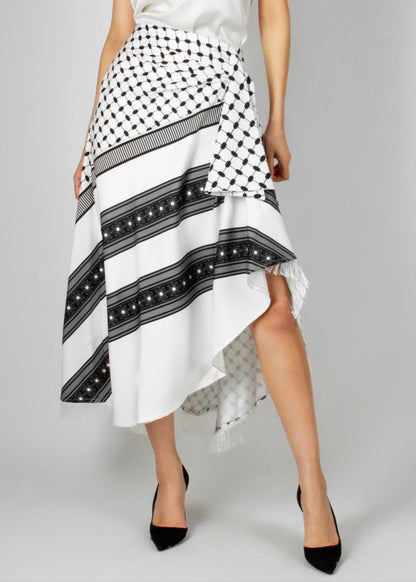 Contemporary white and black asymmetric skirt from the HORRA collection by MNour Design, featuring keffiyeh-inspired patterns and delicate fringe details. Paired with a sleek white sleeveless top for a modern yet culturally rooted look. Explore the collection at www.mnourdesign.com