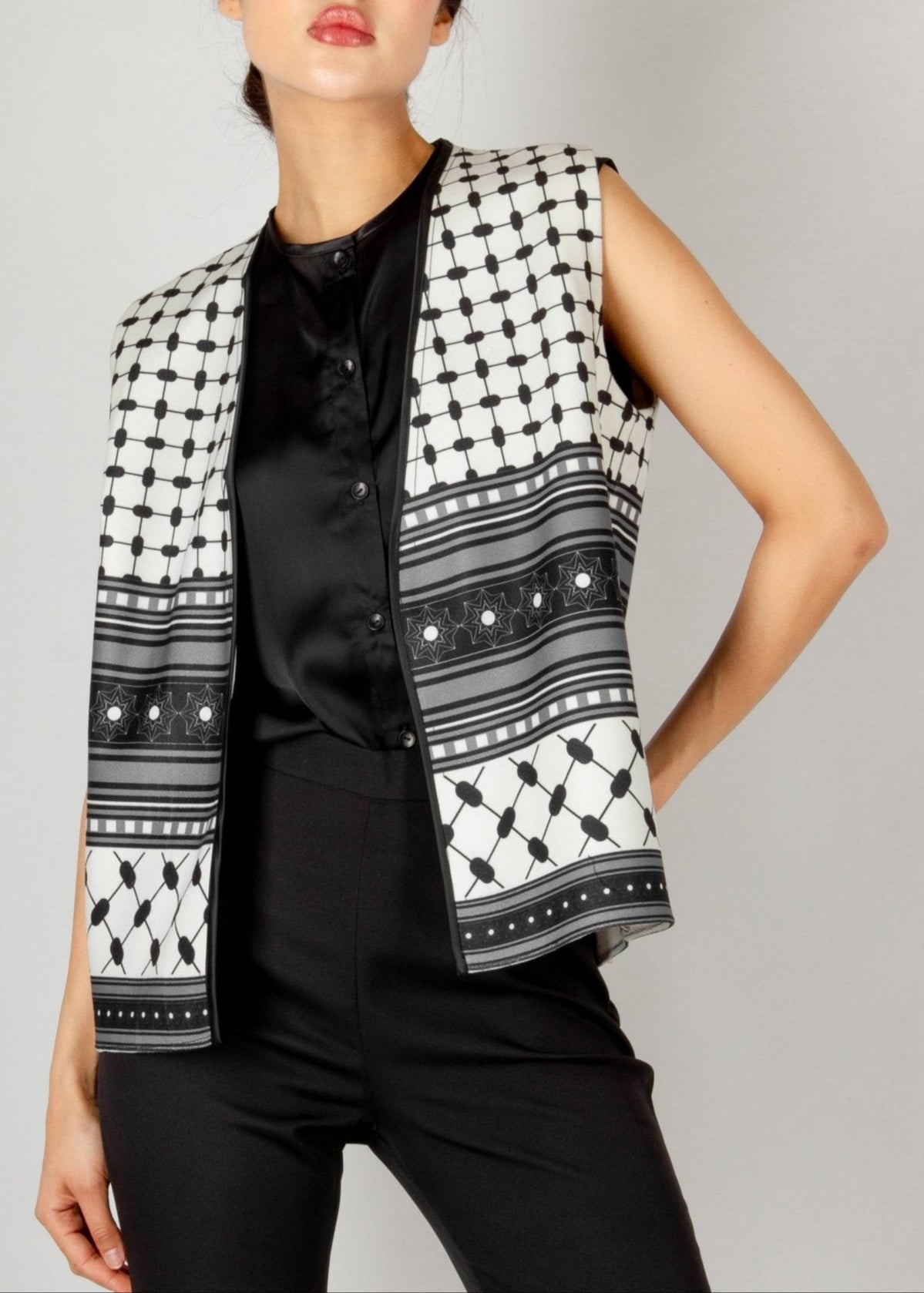 Modern sleeveless vest from the HORRA collection by MNour Design, featuring a striking black-and-white keffiyeh-inspired pattern. Styled with a sleek black satin blouse and tailored trousers for a bold and sophisticated look. Discover more at www.mnourdesign.com
