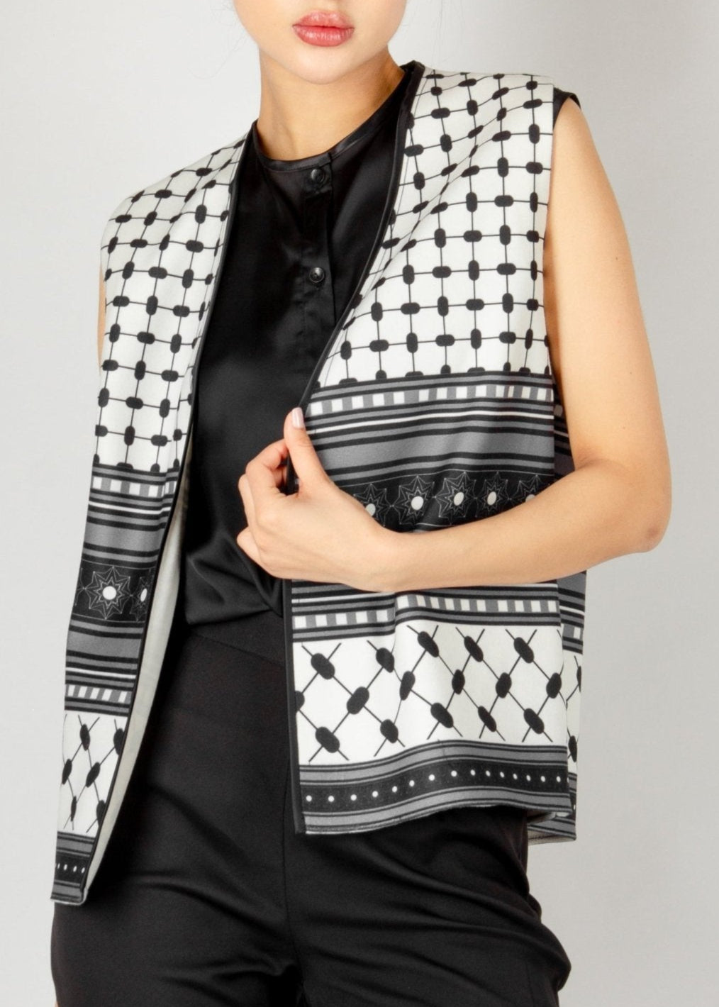 Modern sleeveless vest from the HORRA collection by MNour Design, featuring a striking black-and-white keffiyeh-inspired pattern. Styled with a sleek black satin blouse and tailored trousers for a bold and sophisticated look. Discover more at www.mnourdesign.com