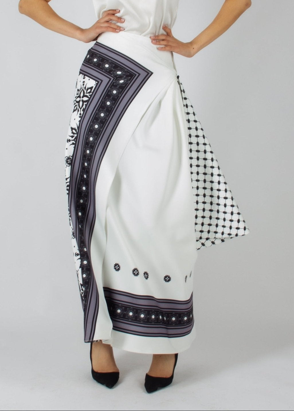 Elegant white maxi skirt from the HORRA collection by MNour Design, featuring intricate traditional-inspired patterns and a draped keffiyeh detail for a bold cultural statement. Paired with a sleek satin top and classic heels for a refined, sophisticated look. Discover more at www.mnourdesign.com
