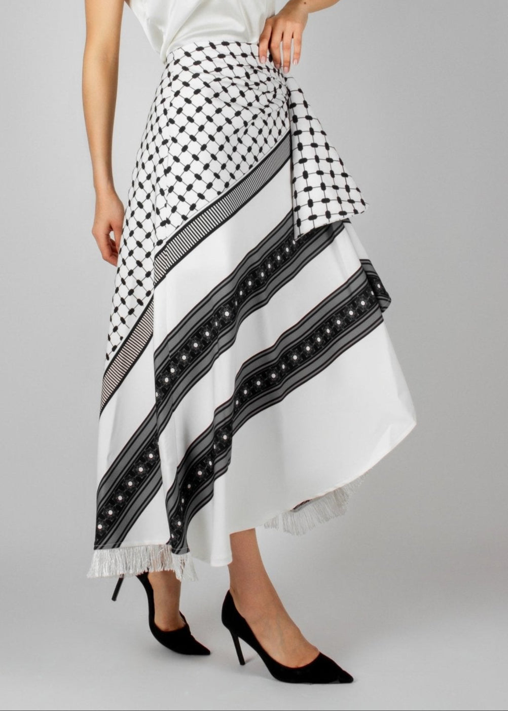 Contemporary white and black asymmetric skirt from the HORRA collection by MNour Design, featuring keffiyeh-inspired patterns and delicate fringe details. Paired with a sleek white sleeveless top for a modern yet culturally rooted look. Explore the collection at www.mnourdesign.com