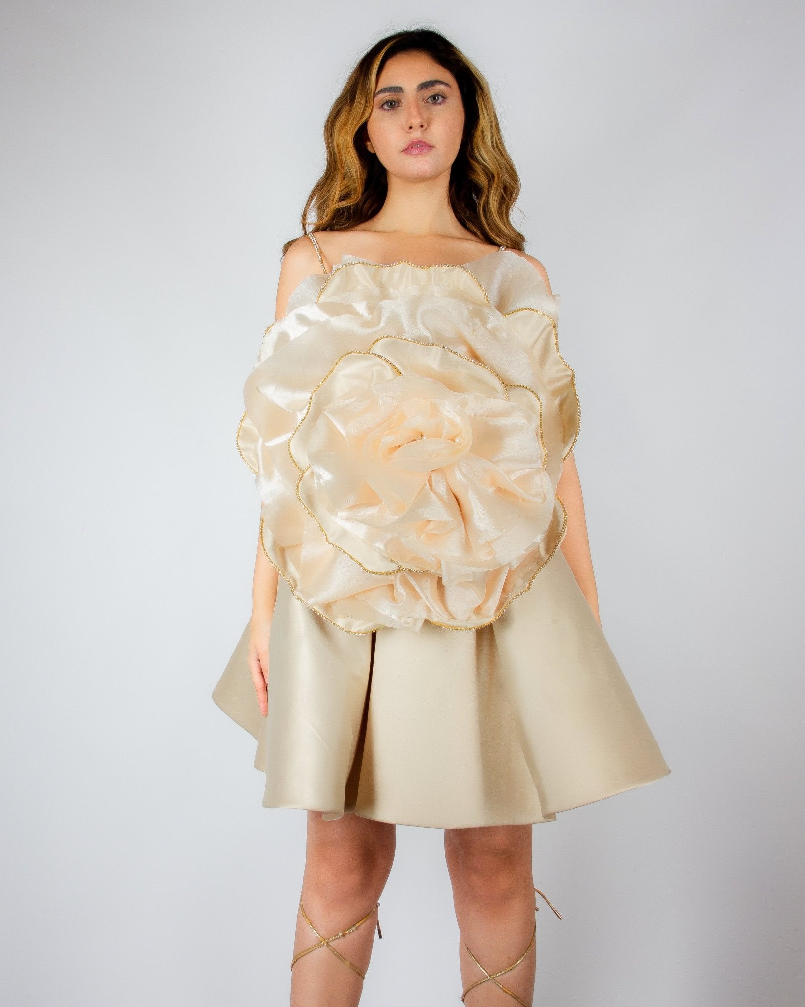 Luxurious champagne-colored mini dress by MNour Design, featuring a voluminous satin skirt and an oversized sculptural rose detail on the bodice with gold-trimmed petals. A bold, artistic statement for elegant occasions. Discover this exclusive couture piece at www.mnourdesign.com.