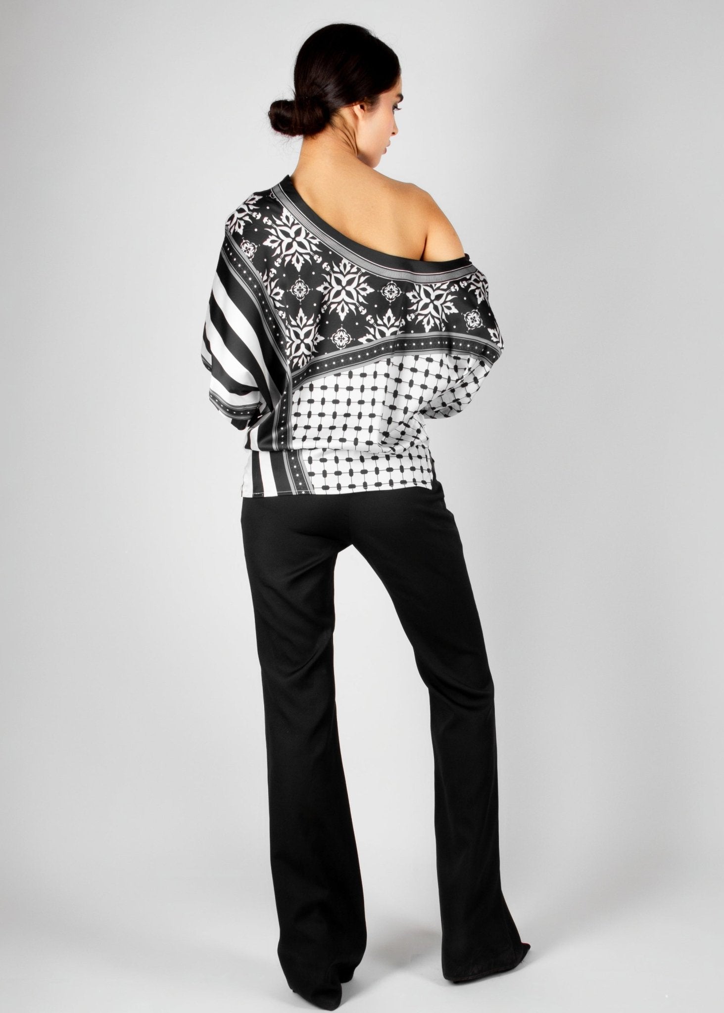 Bold off-shoulder blouse from the HORRA collection by MNour Design, featuring a striking keffiyeh-inspired pattern with intricate geometric details. Paired with sleek black trousers for a modern, sophisticated look. Explore more at www.mnourdesign.com