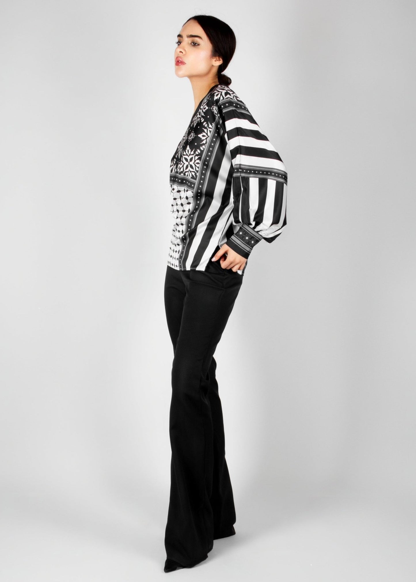 Bold off-shoulder blouse from the HORRA collection by MNour Design, featuring a striking keffiyeh-inspired pattern with intricate geometric details. Paired with sleek black trousers for a modern, sophisticated look. Explore more at www.mnourdesign.com
