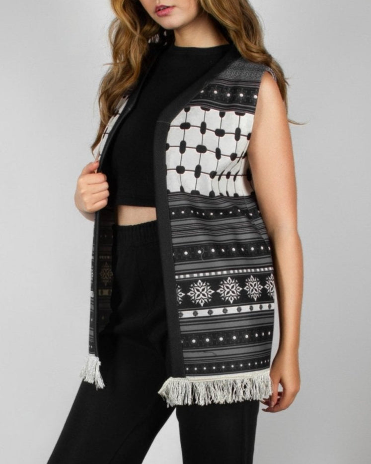Modern black and white vest from the HORRA collection by MNour Design, featuring intricate geometric and traditional patterns with delicate fringe detailing. Styled over a sleek black ensemble for a contemporary yet culturally inspired look. Discover more at www.mnourdesign.com
