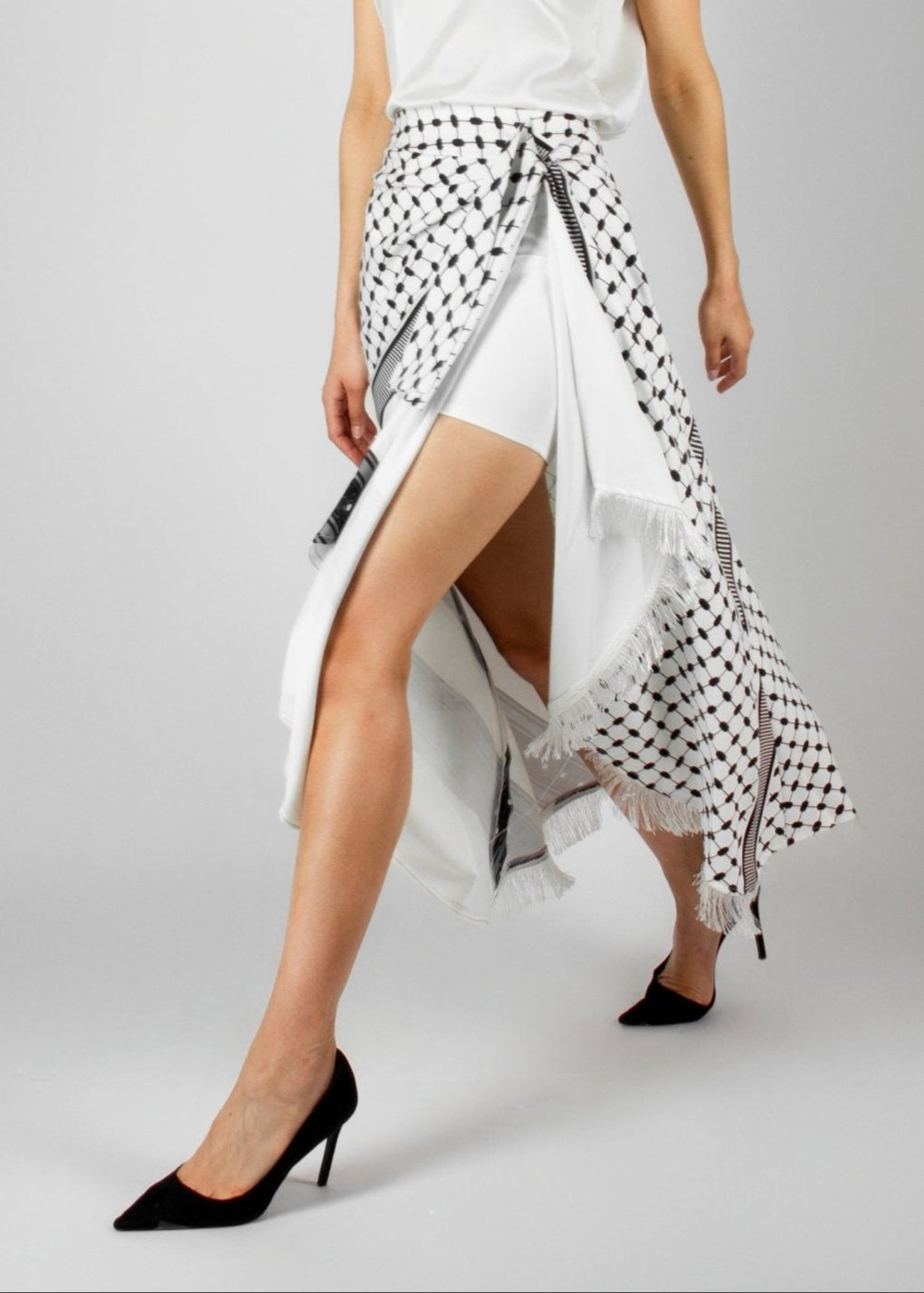 Contemporary white and black asymmetric skirt from the HORRA collection by MNour Design, featuring keffiyeh-inspired patterns and delicate fringe details. Paired with a sleek white sleeveless top for a modern yet culturally rooted look. Explore the collection at www.mnourdesign.com