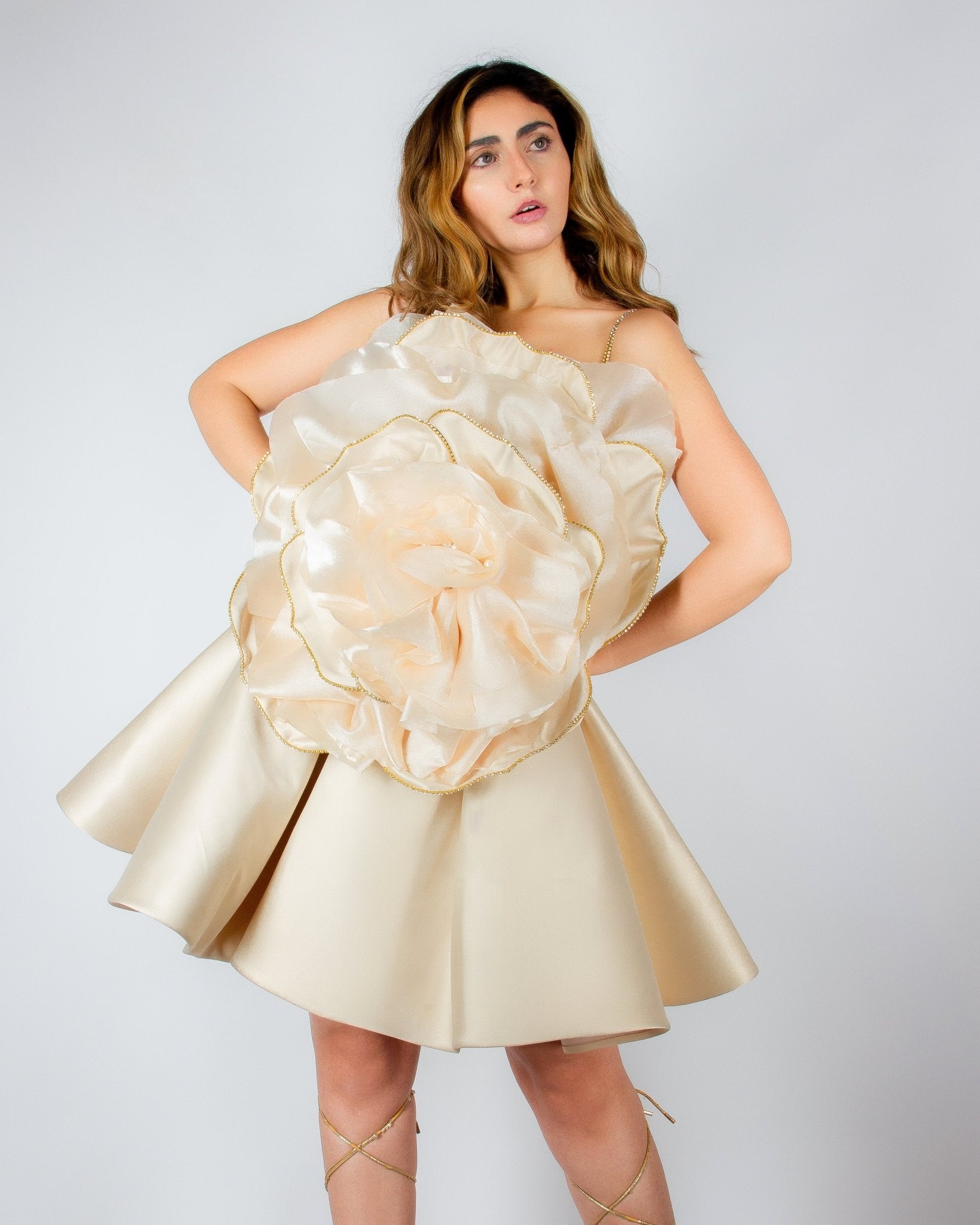 Luxurious champagne-colored mini dress by MNour Design, featuring a voluminous satin skirt and an oversized sculptural rose detail on the bodice with gold-trimmed petals. A bold, artistic statement for elegant occasions. Discover this exclusive couture piece at www.mnourdesign.com.