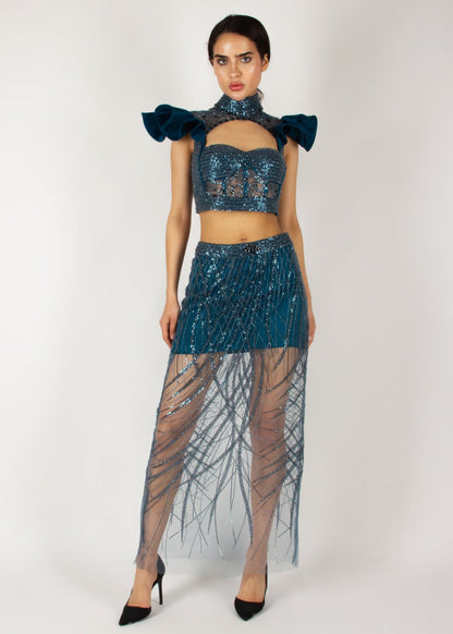 Elegant two-piece couture set by MNour Design, featuring a shimmering blue embellished crop top with dramatic ruffled shoulders and a high-neck cut, paired with a matching sheer beaded skirt for a bold and sophisticated look. Explore this stunning design at www.mnourdesign.com.