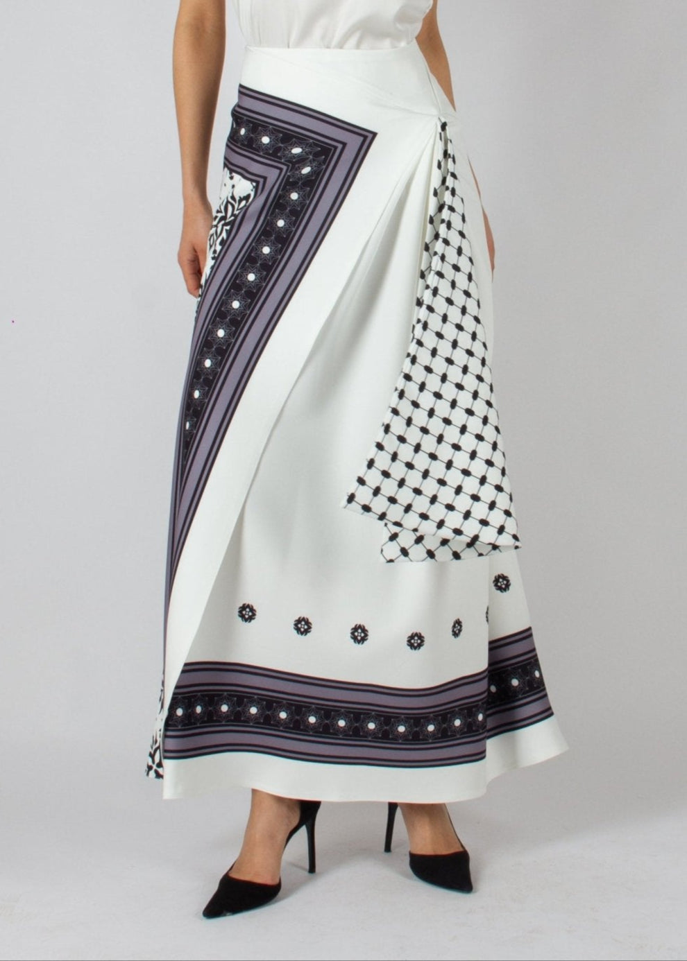 Elegant white maxi skirt from the HORRA collection by MNour Design, featuring intricate traditional-inspired patterns and a draped keffiyeh detail for a bold cultural statement. Paired with a sleek satin top and classic heels for a refined, sophisticated look. Discover more at www.mnourdesign.com