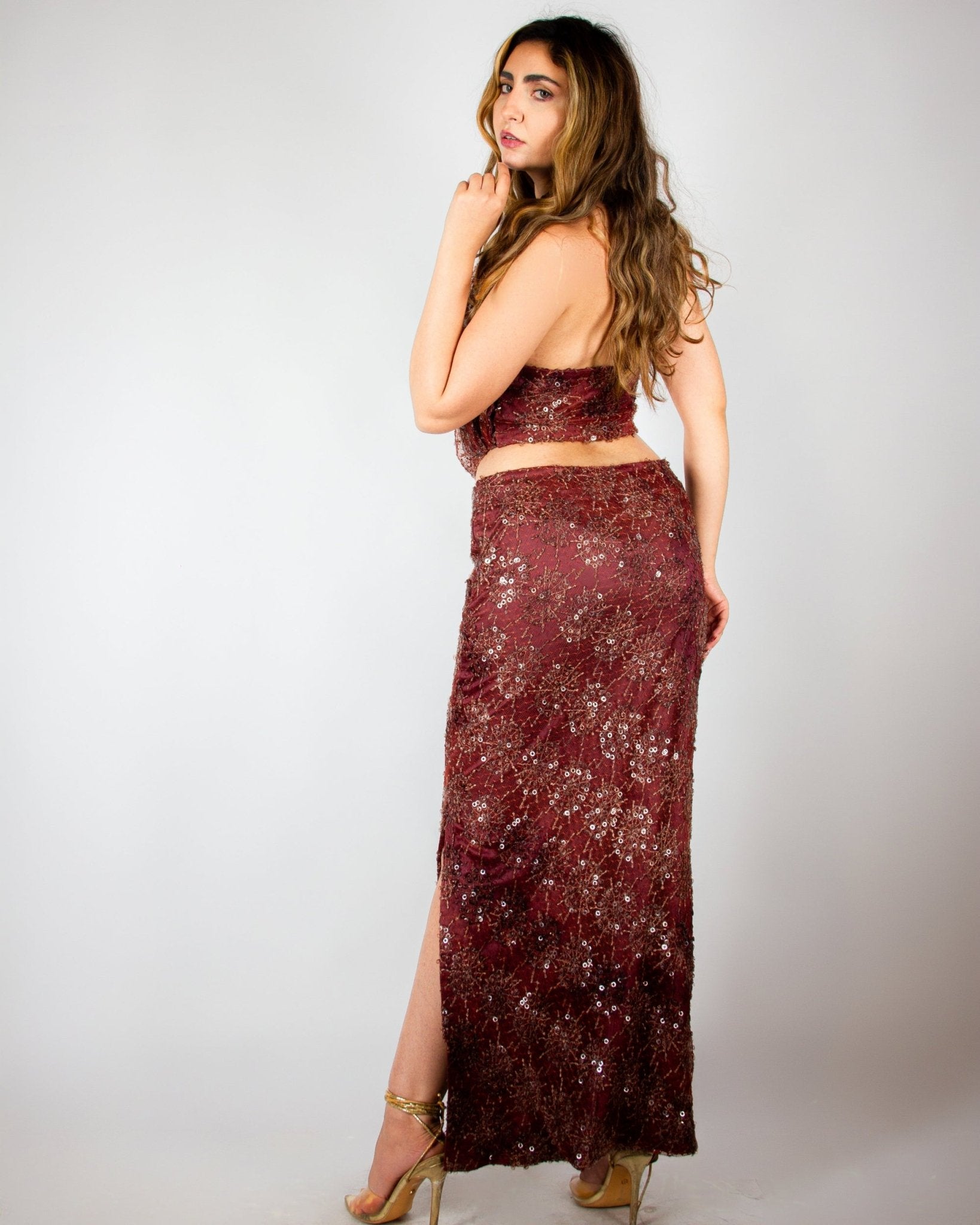Elegant two-piece evening ensemble by MNour Design, featuring a shimmering burgundy sequined skirt with a high slit and a draped cowl-neck crop top. The intricate beadwork and rich fabric exude sophistication and modern glamour. Shop this exclusive design at www.mnourdesign.com