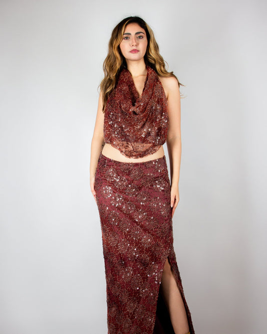 Elegant two-piece evening ensemble by MNour Design, featuring a shimmering burgundy sequined skirt with a high slit and a draped cowl-neck crop top. The intricate beadwork and rich fabric exude sophistication and modern glamour. Shop this exclusive design at www.mnourdesign.com