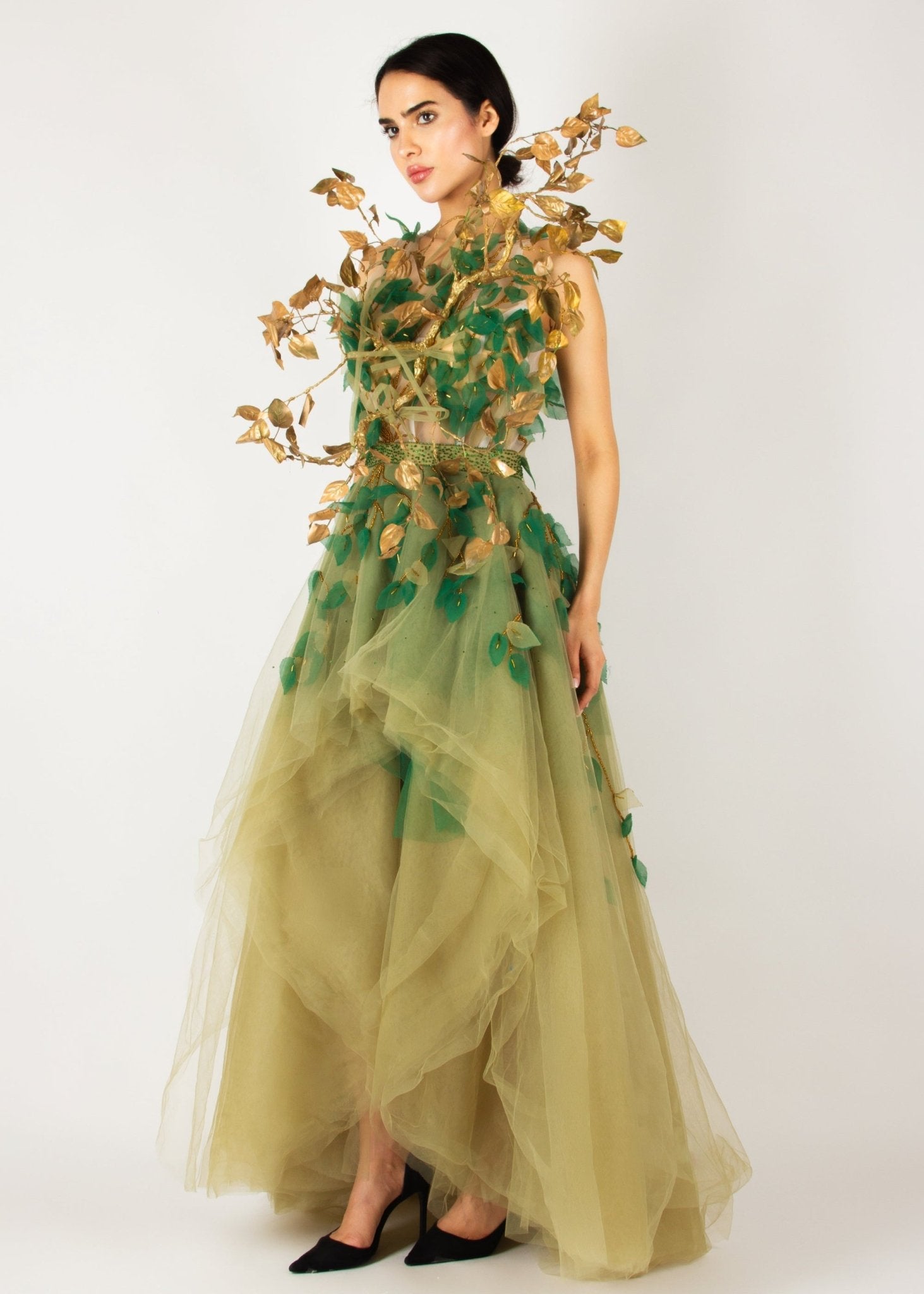 Enchanting nature-inspired gown by MNour Design, featuring a flowing olive-green tulle skirt with a high-low cut and an intricately designed bodice adorned with gold and green leaf appliqués. A breathtaking fusion of fashion and artistry. Discover this exclusive design at www.mnourdesign.com