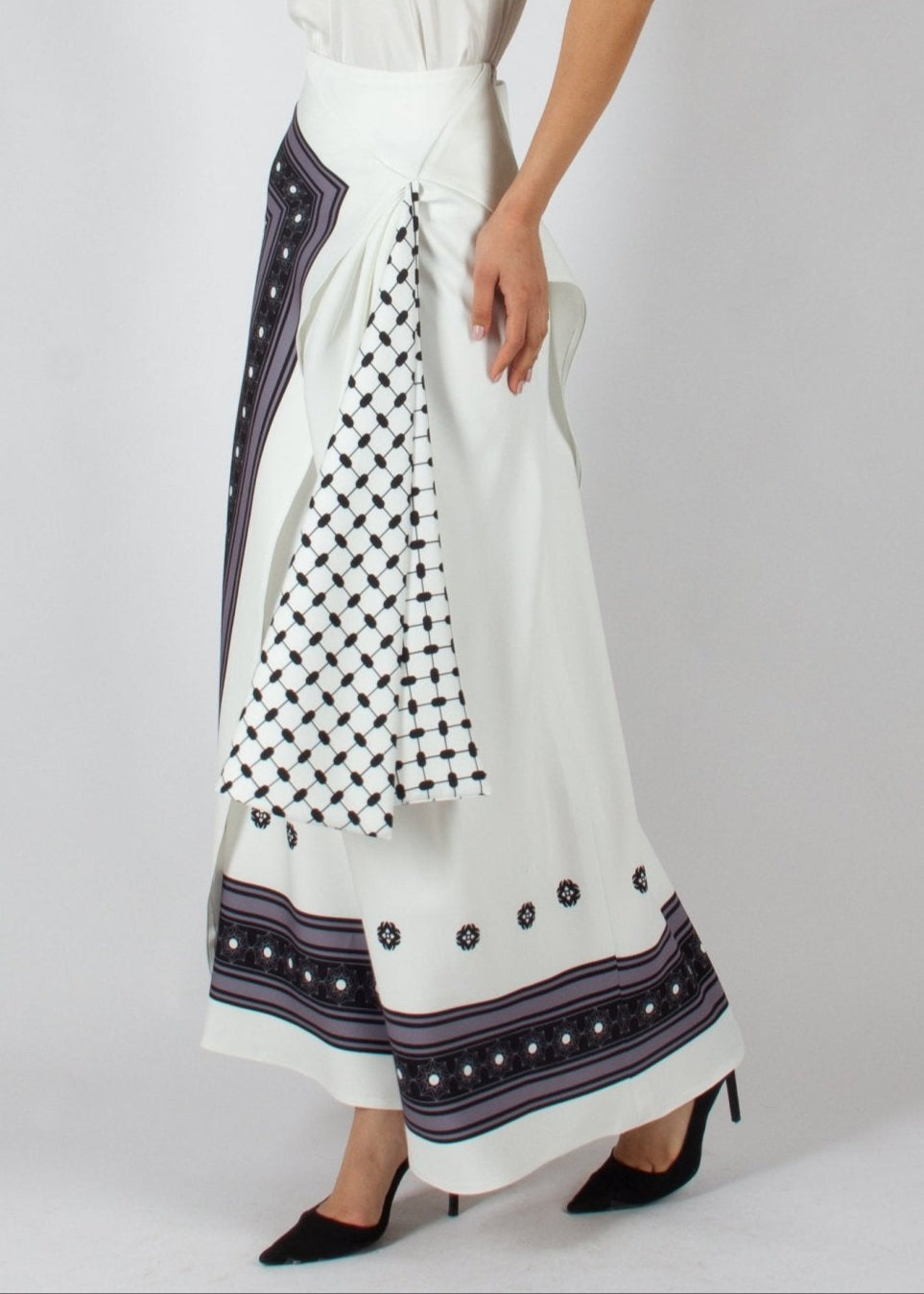 Elegant white maxi skirt from the HORRA collection by MNour Design, featuring intricate traditional-inspired patterns and a draped keffiyeh detail for a bold cultural statement. Paired with a sleek satin top and classic heels for a refined, sophisticated look. Discover more at www.mnourdesign.com