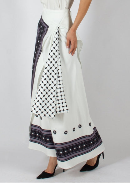 Elegant white maxi skirt from the HORRA collection by MNour Design, featuring intricate traditional-inspired patterns and a draped keffiyeh detail for a bold cultural statement. Paired with a sleek satin top and classic heels for a refined, sophisticated look. Discover more at www.mnourdesign.com