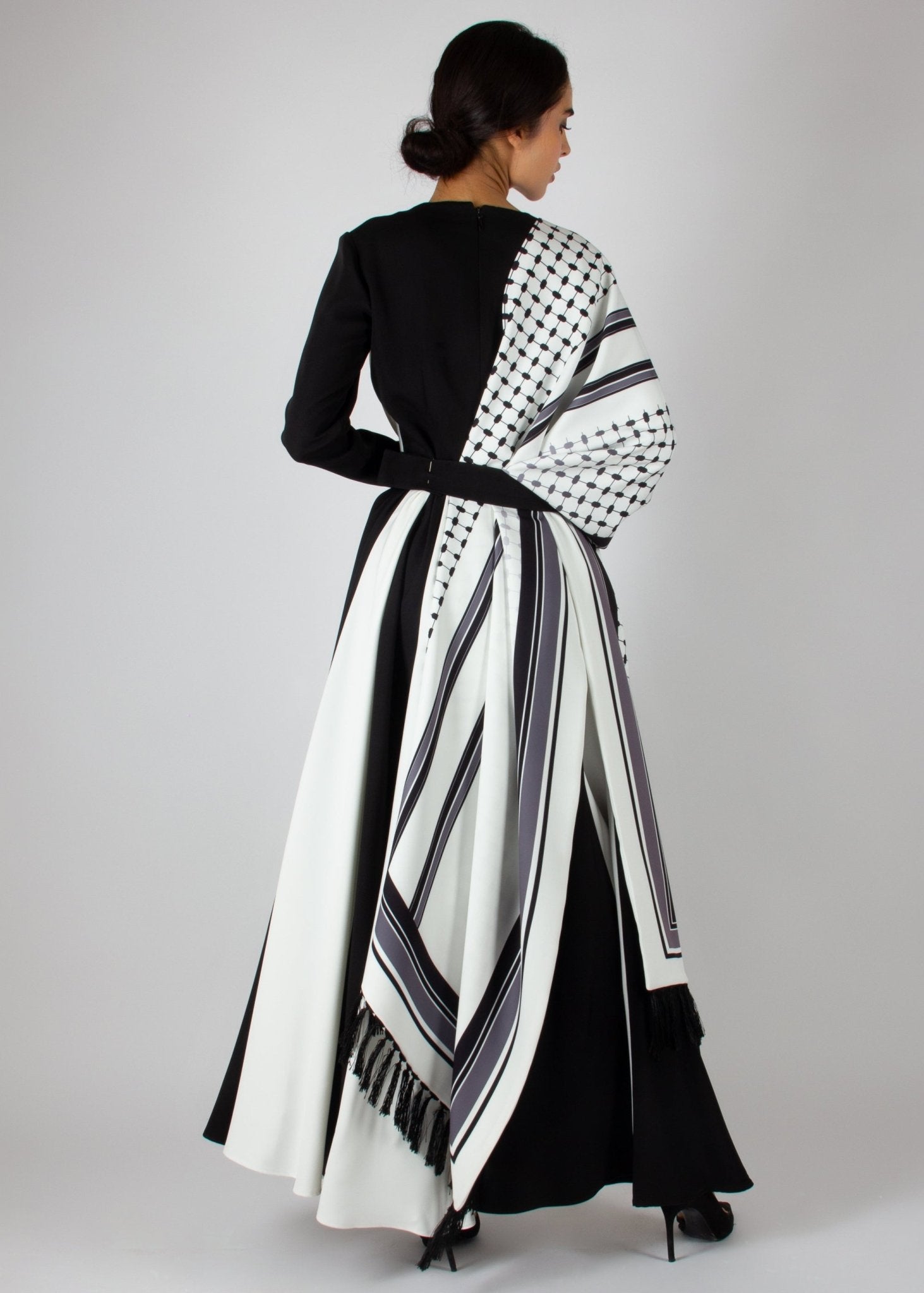 Flowing black and white wrap dress from the HORRA collection by MNour Design, featuring keffiyeh-inspired prints and elegant fringe details. A statement piece blending cultural heritage with modern sophistication. Discover more at www.mnourdesign.com