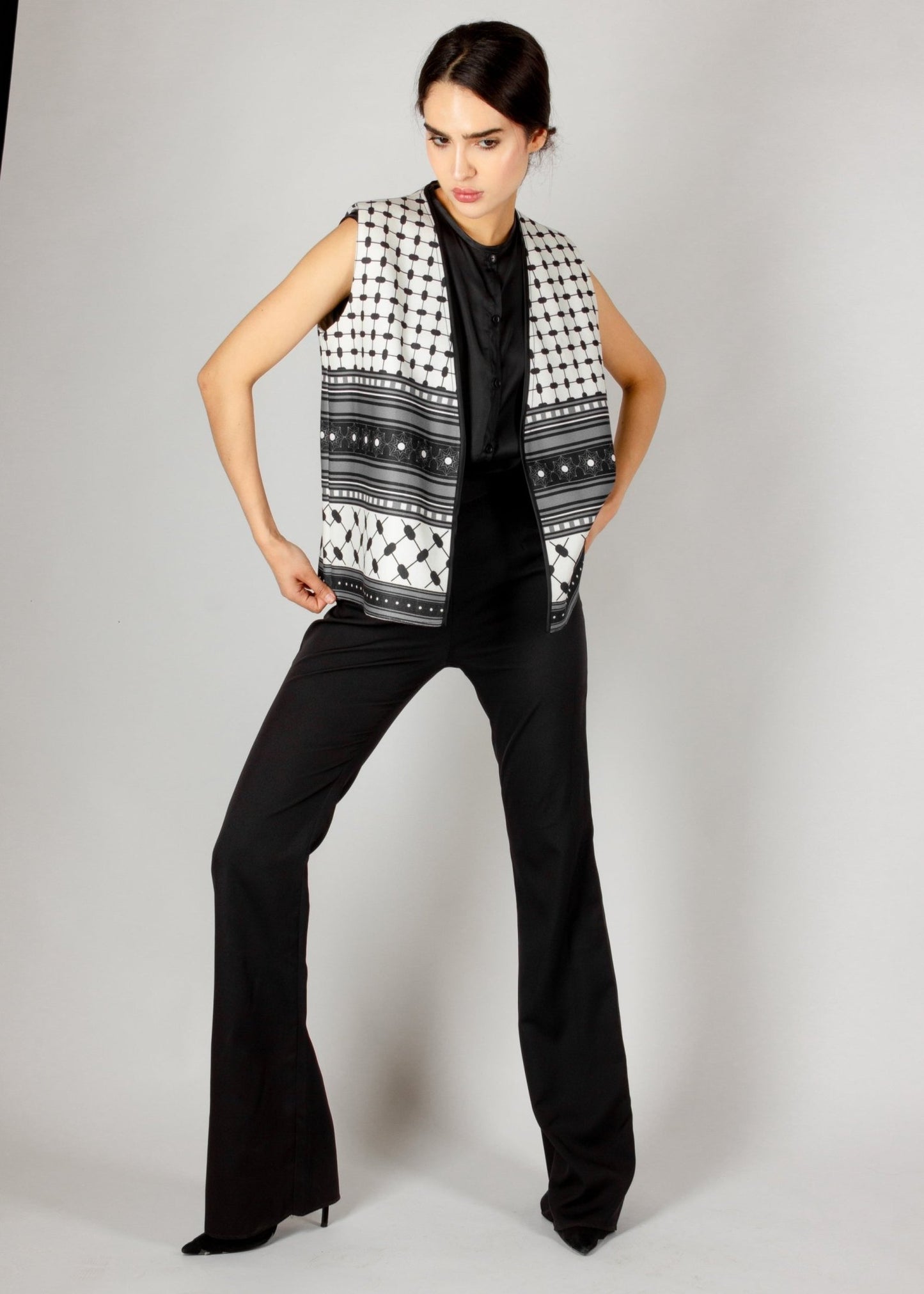 Modern sleeveless vest from the HORRA collection by MNour Design, featuring a striking black-and-white keffiyeh-inspired pattern. Styled with a sleek black satin blouse and tailored trousers for a bold and sophisticated look. Discover more at www.mnourdesign.com