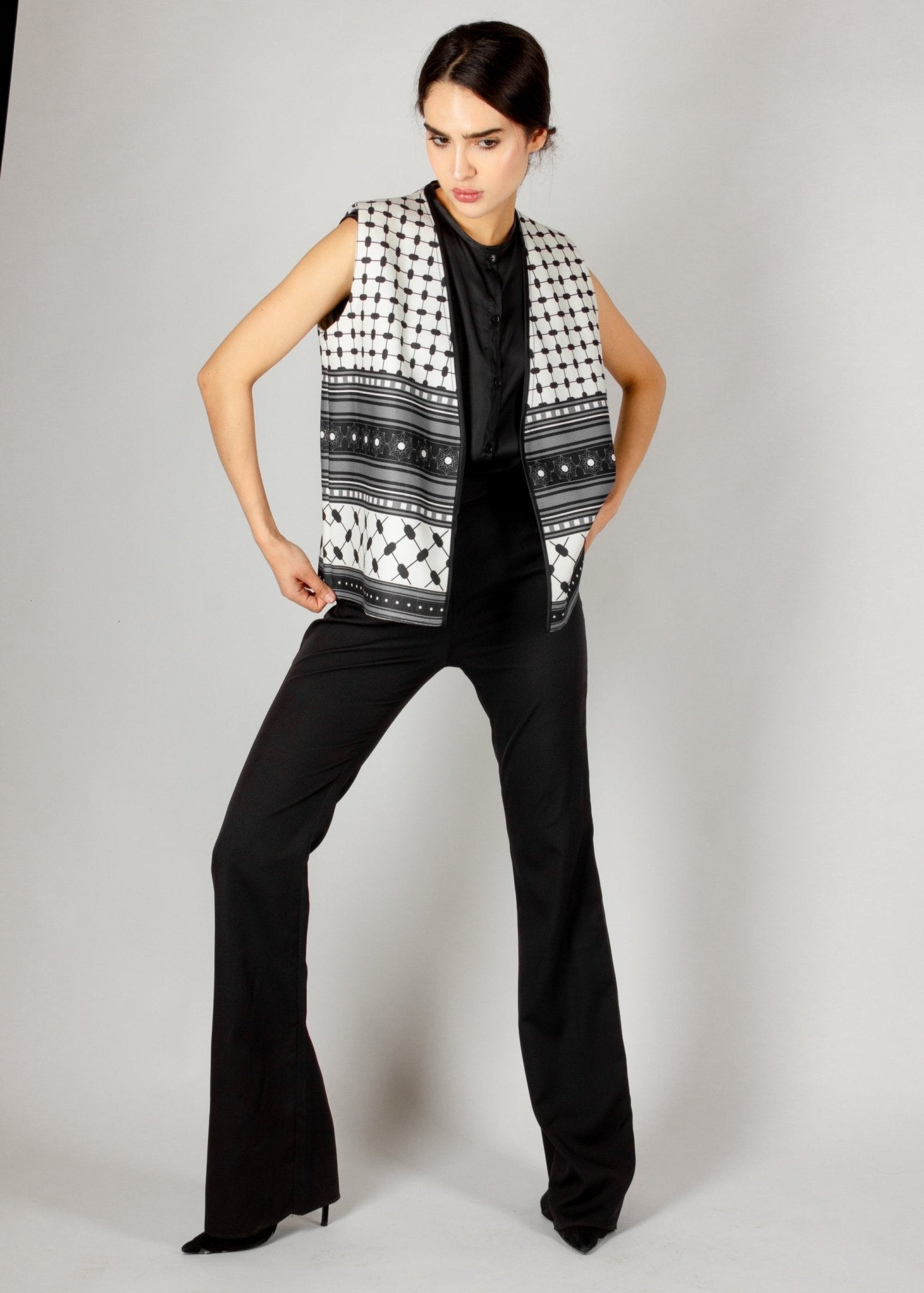 Modern sleeveless vest from the HORRA collection by MNour Design, featuring a striking black-and-white keffiyeh-inspired pattern. Styled with a sleek black satin blouse and tailored trousers for a bold and sophisticated look. Discover more at www.mnourdesign.com
