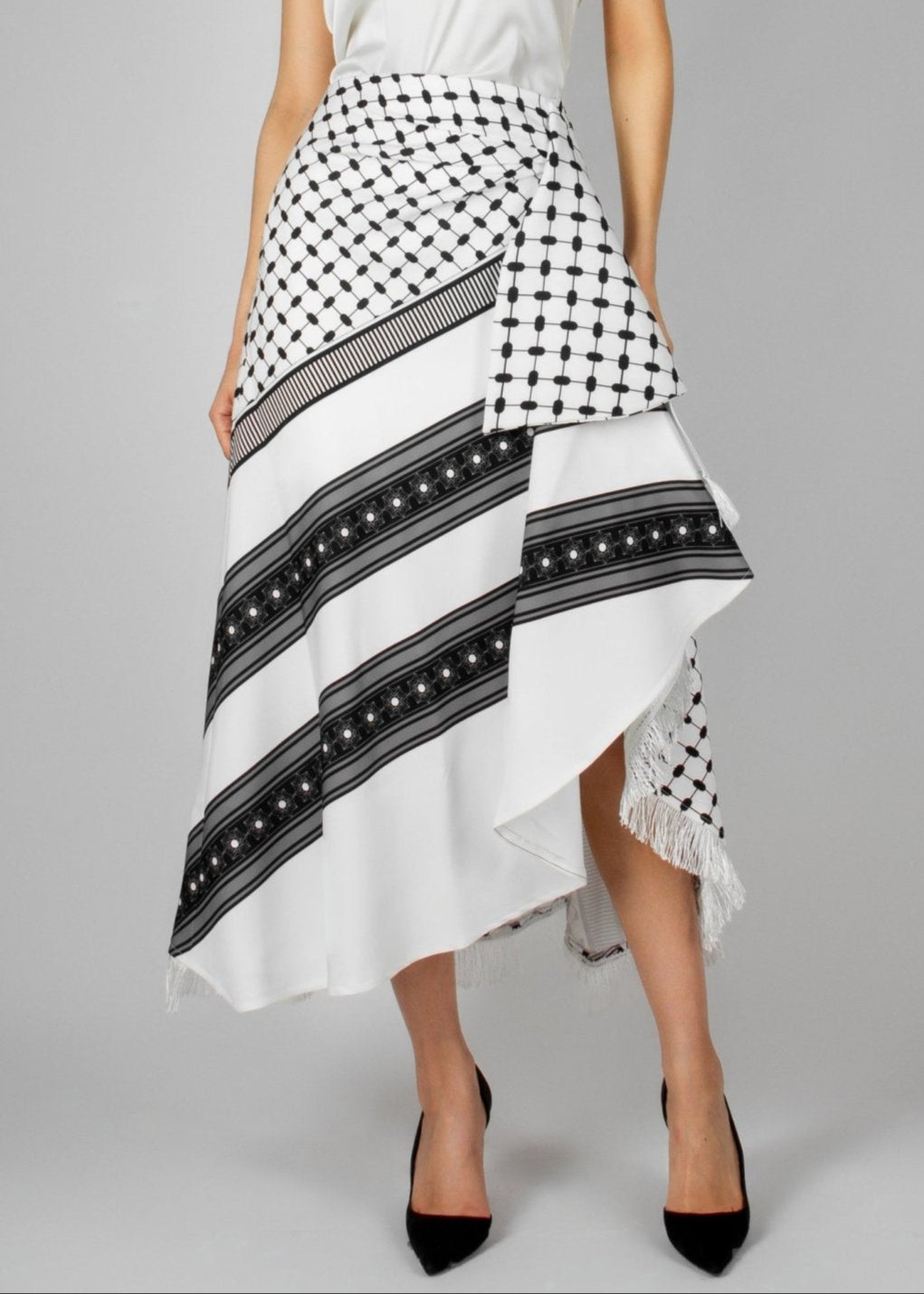Contemporary white and black asymmetric skirt from the HORRA collection by MNour Design, featuring keffiyeh-inspired patterns and delicate fringe details. Paired with a sleek white sleeveless top for a modern yet culturally rooted look. Explore the collection at www.mnourdesign.com