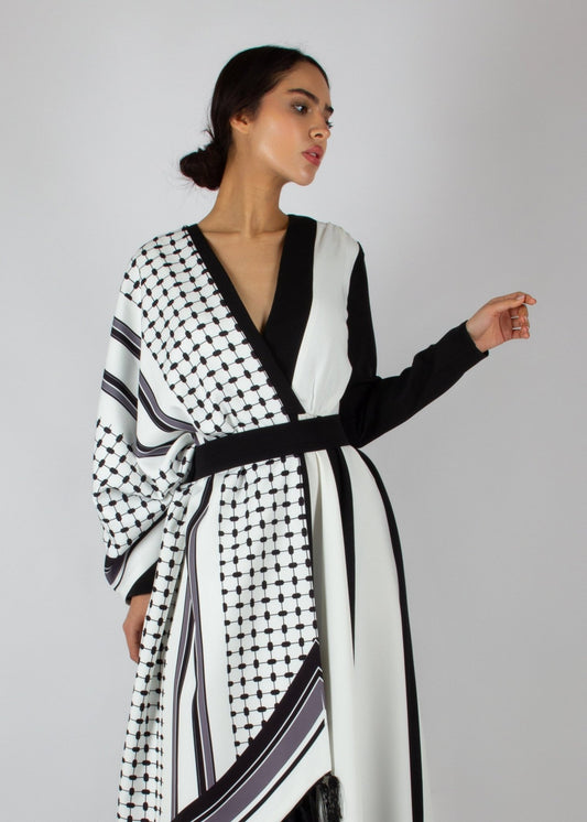 Flowing black and white wrap dress from the HORRA collection by MNour Design, featuring keffiyeh-inspired prints and elegant fringe details. A statement piece blending cultural heritage with modern sophistication. Discover more at www.mnourdesign.com