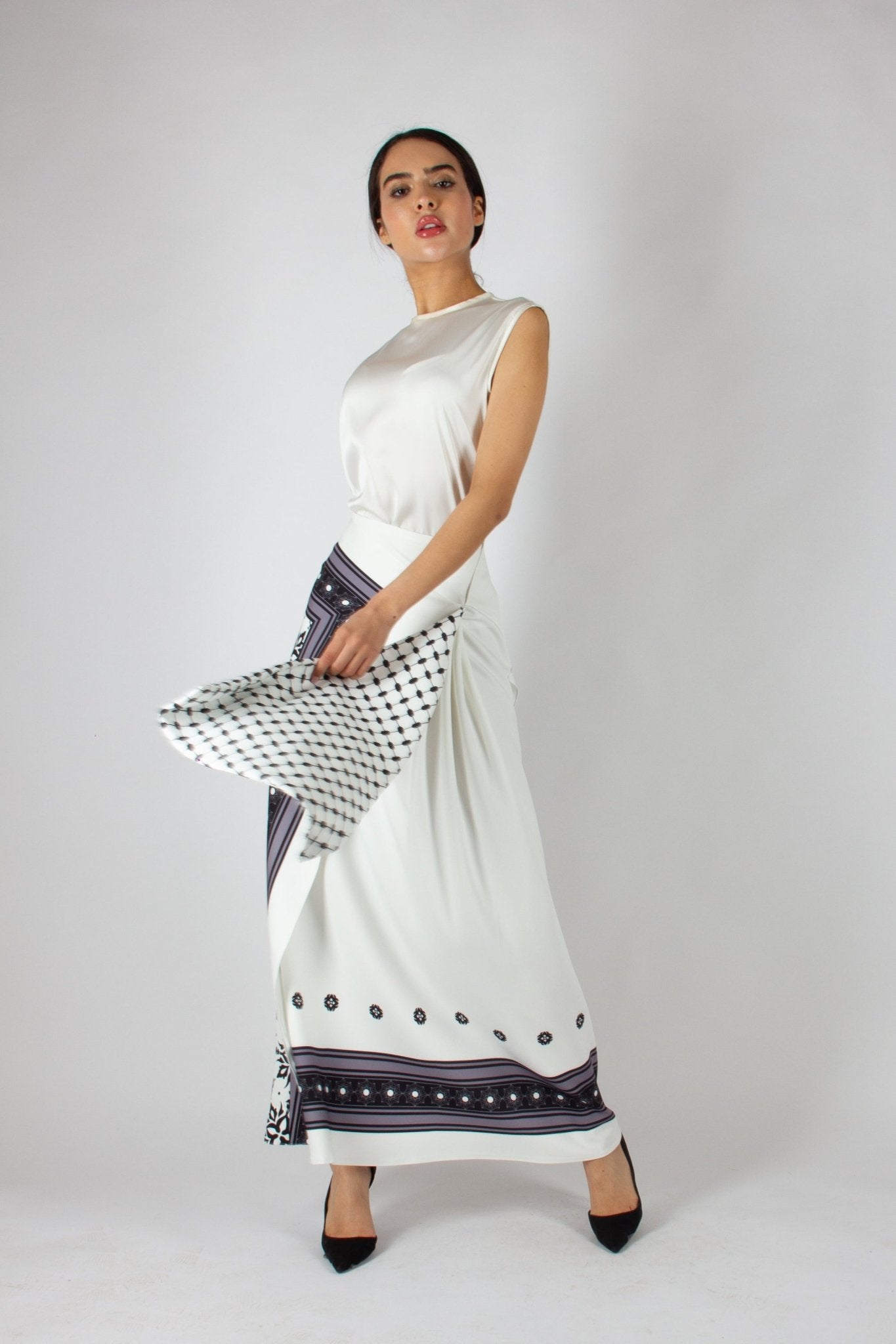 Elegant white maxi skirt from the HORRA collection by MNour Design, featuring intricate traditional-inspired patterns and a draped keffiyeh detail for a bold cultural statement. Paired with a sleek satin top and classic heels for a refined, sophisticated look. Discover more at www.mnourdesign.com